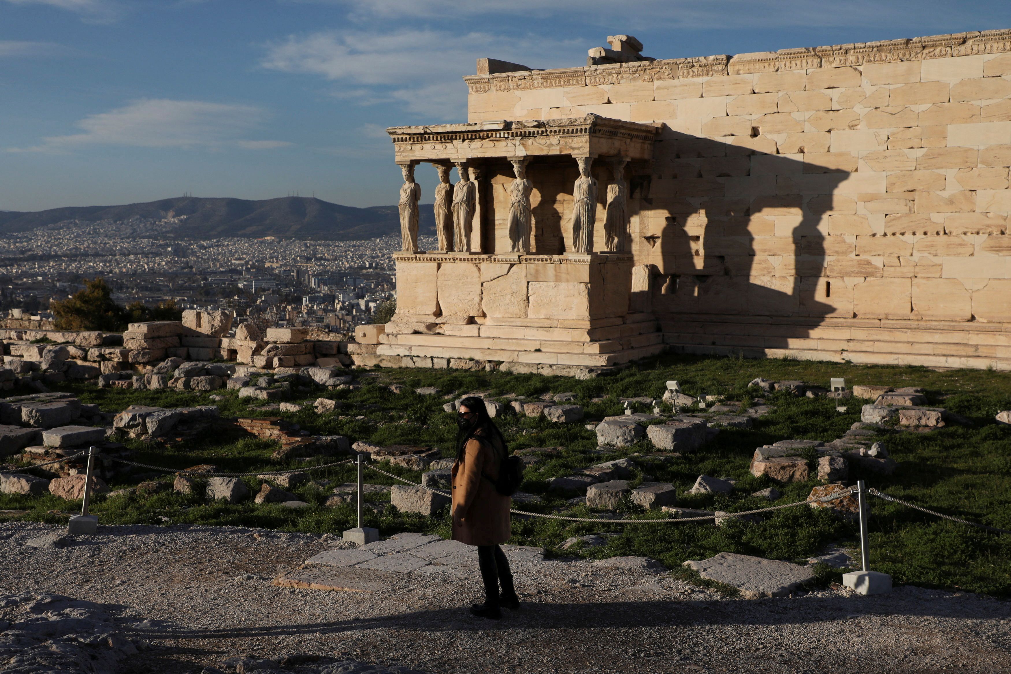 A woman wearing a protective face mask makes her way in front of the ancient Erechtheion temple, in Athens