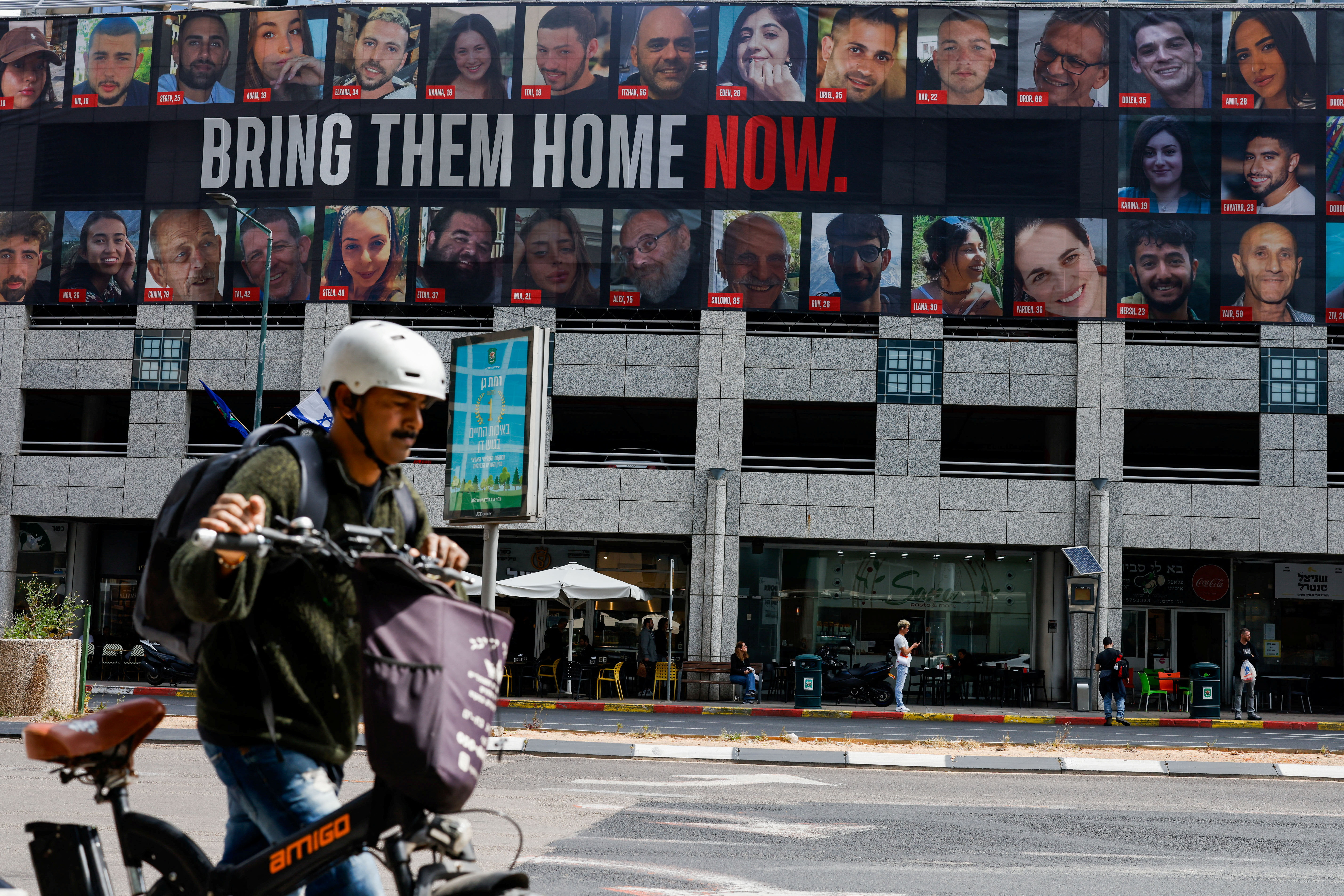 Man pushes a bike near a billboard with pictures of hostages kidnapped in the deadly October 7 attack on Israel by Hamas, in Tel Aviv