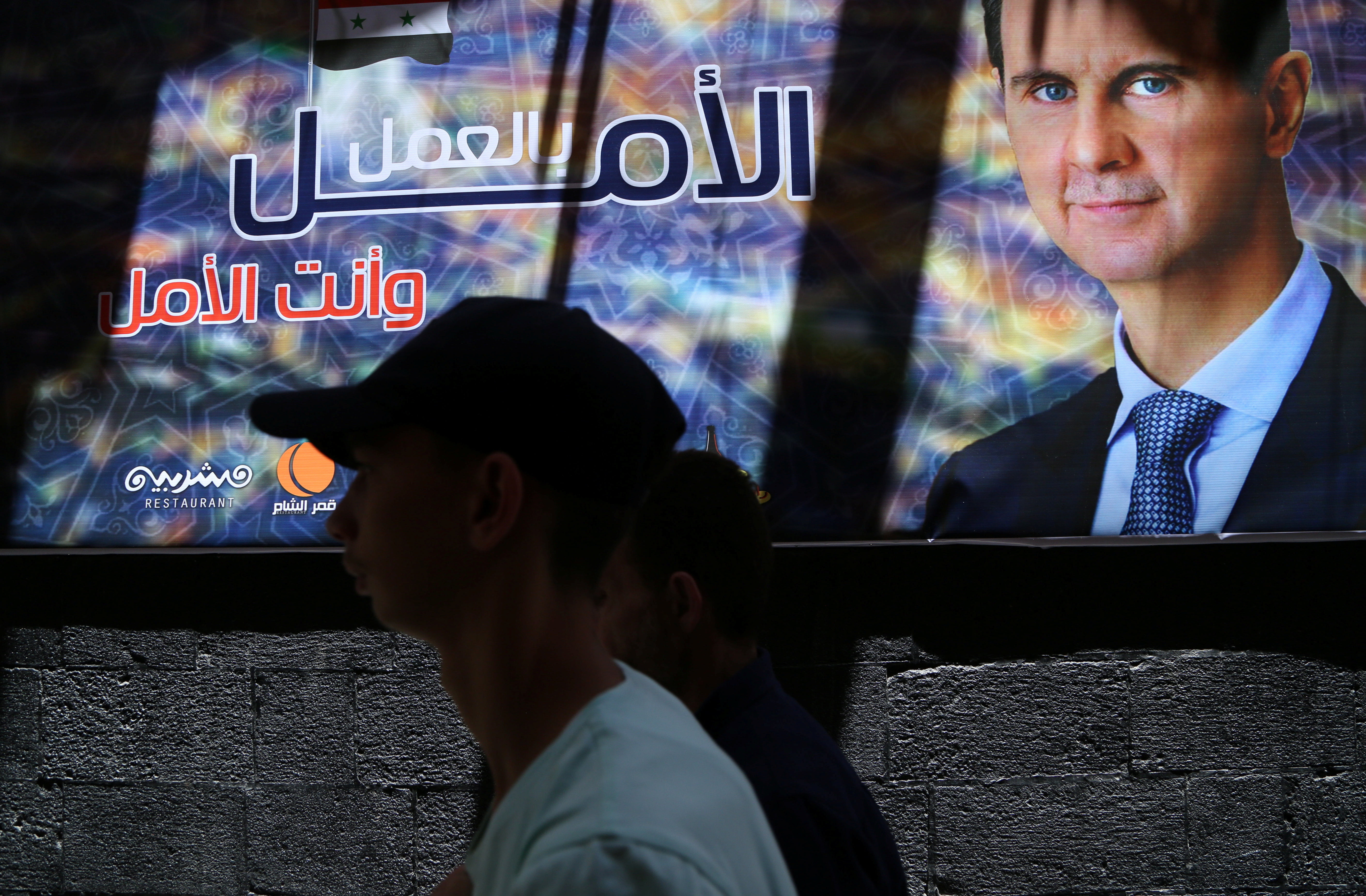 A man walks past a banner depicting Syria's President Bashar al-Assad in Damascus