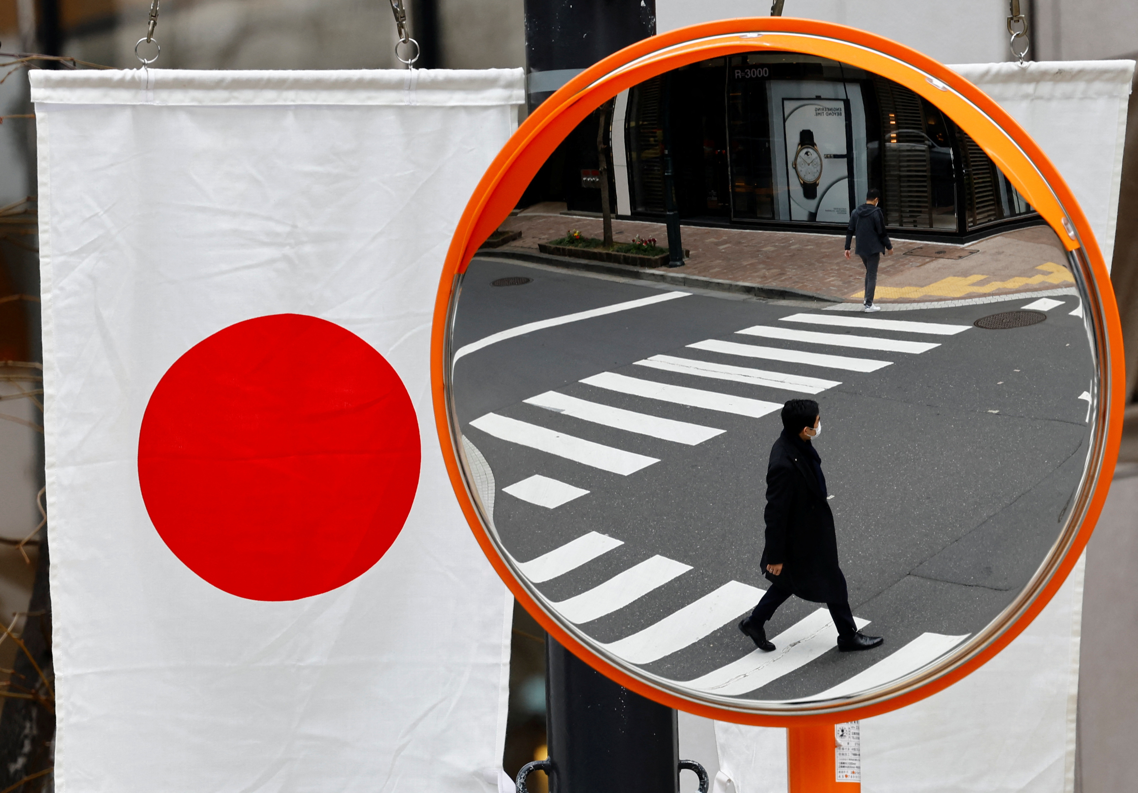Pedestrians are reflected on a curved mirror next to Japan’s national flag in Tokyo