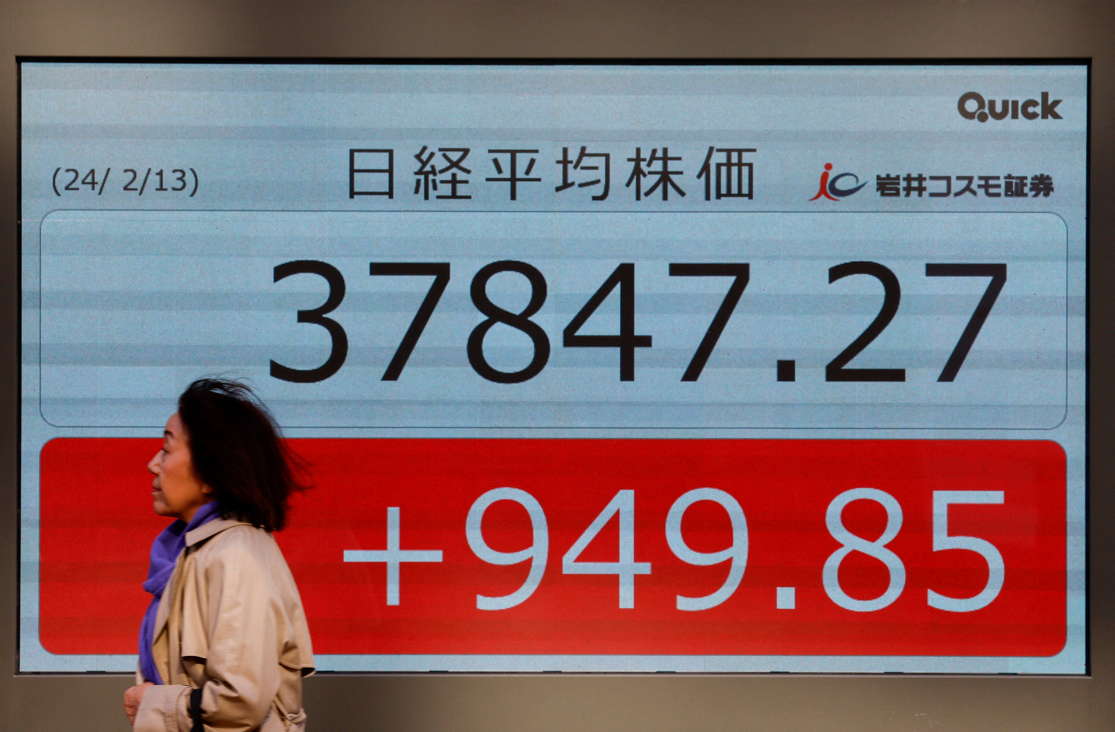 A passerby walks past in front of an electric screen displaying Japan's Nikkei share average outside a brokerage in Tokyo