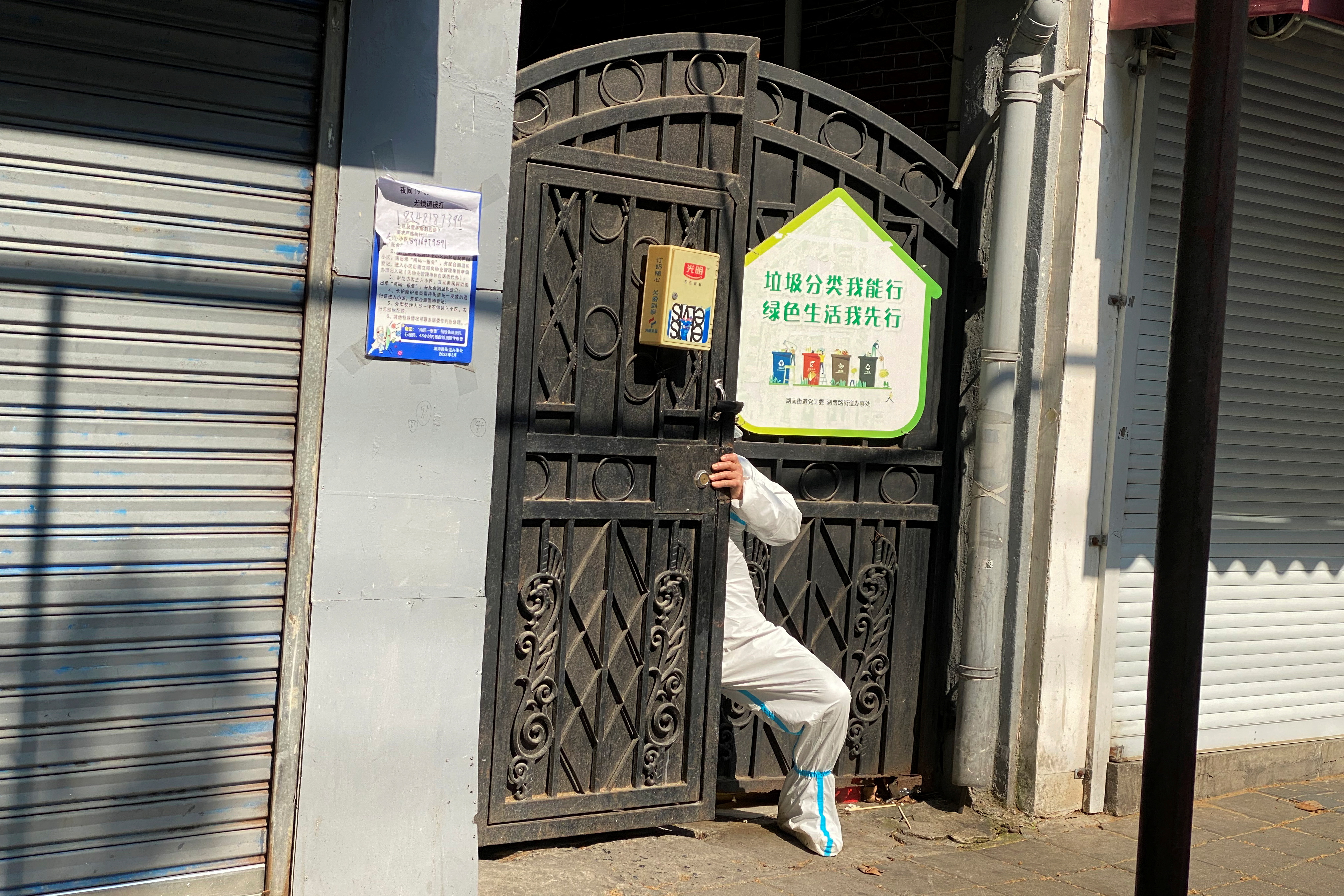 Person in a protective suit squeezes through a locked gate of a residential compound, following the coronavirus disease (COVID-19) outbreak in Shanghai