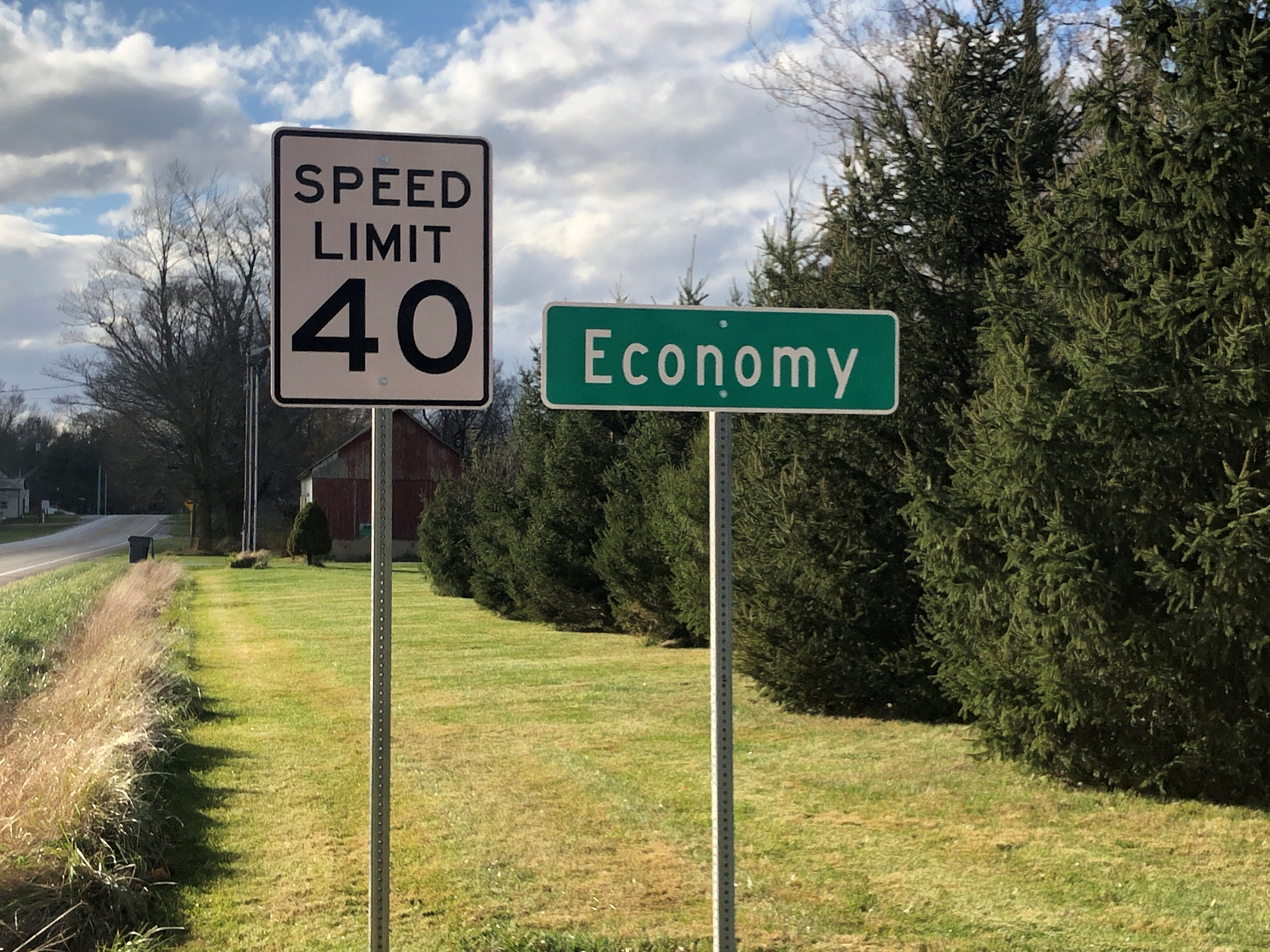 A speed limit sign is seen beside a city sign for Economy, Indiana