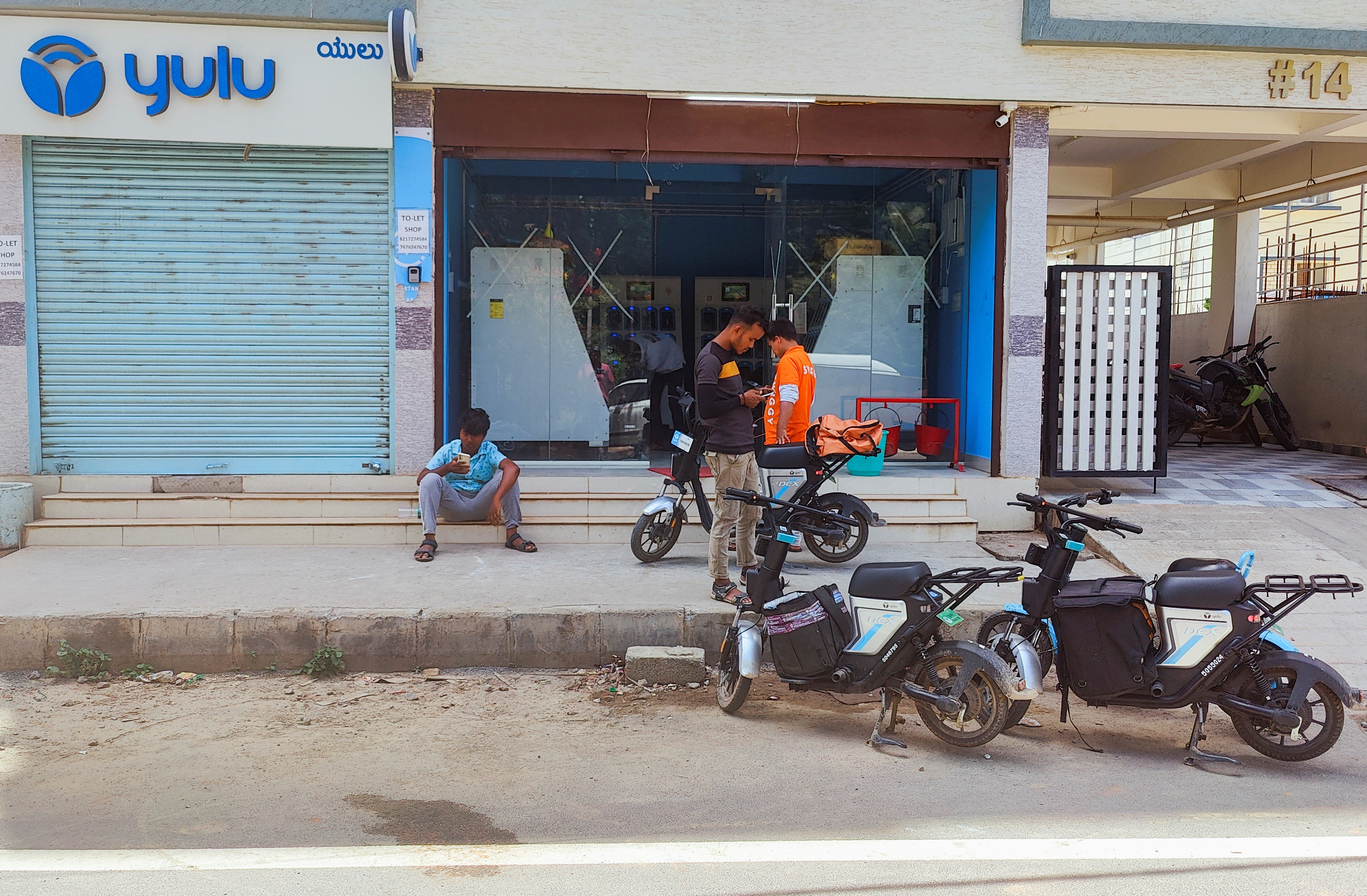 Food delivery agents await for recharged battery packs outside a Yulu recharge station, in Bengaluru