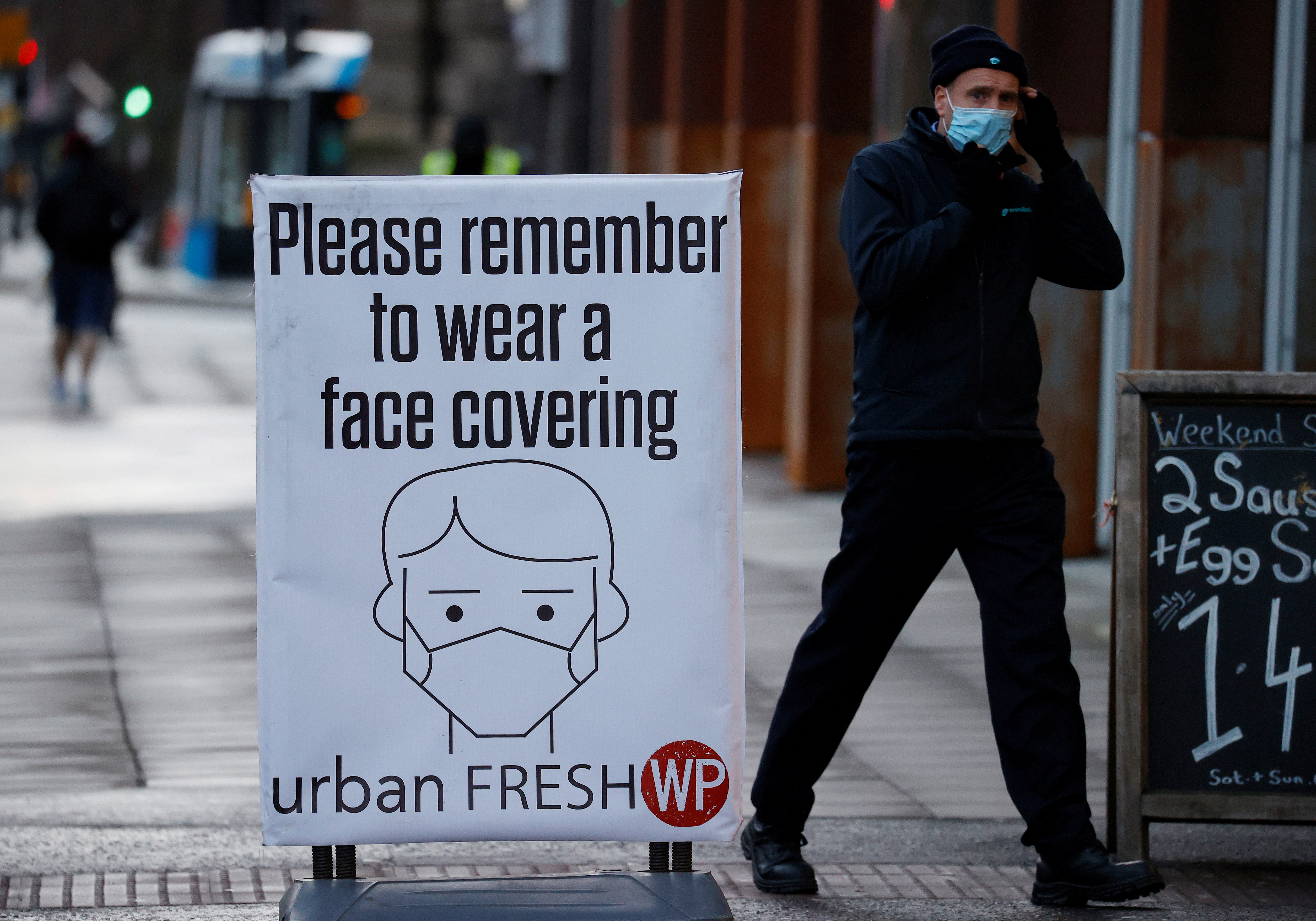 A man walks past a sign encouraging people to wear face coverings amid the COVID-19 outbreak in Belfast, Northern Ireland January 2, 2021. REUTERS/Phil Noble/Files