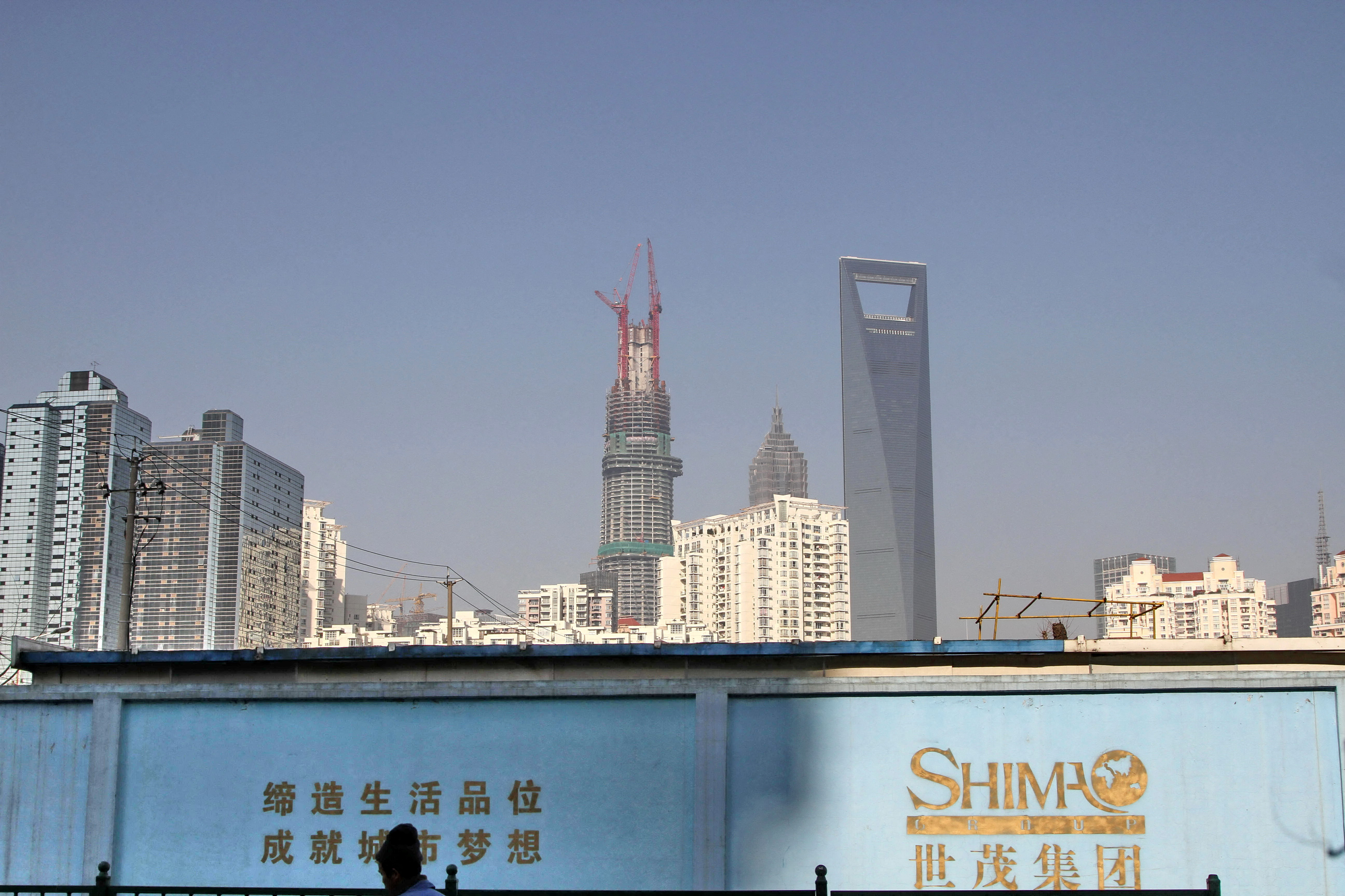 Man walks past a wall carrying the logo of Shimao Group, with residential buildings and the financial district of Pudong seen in the background, in Shanghai