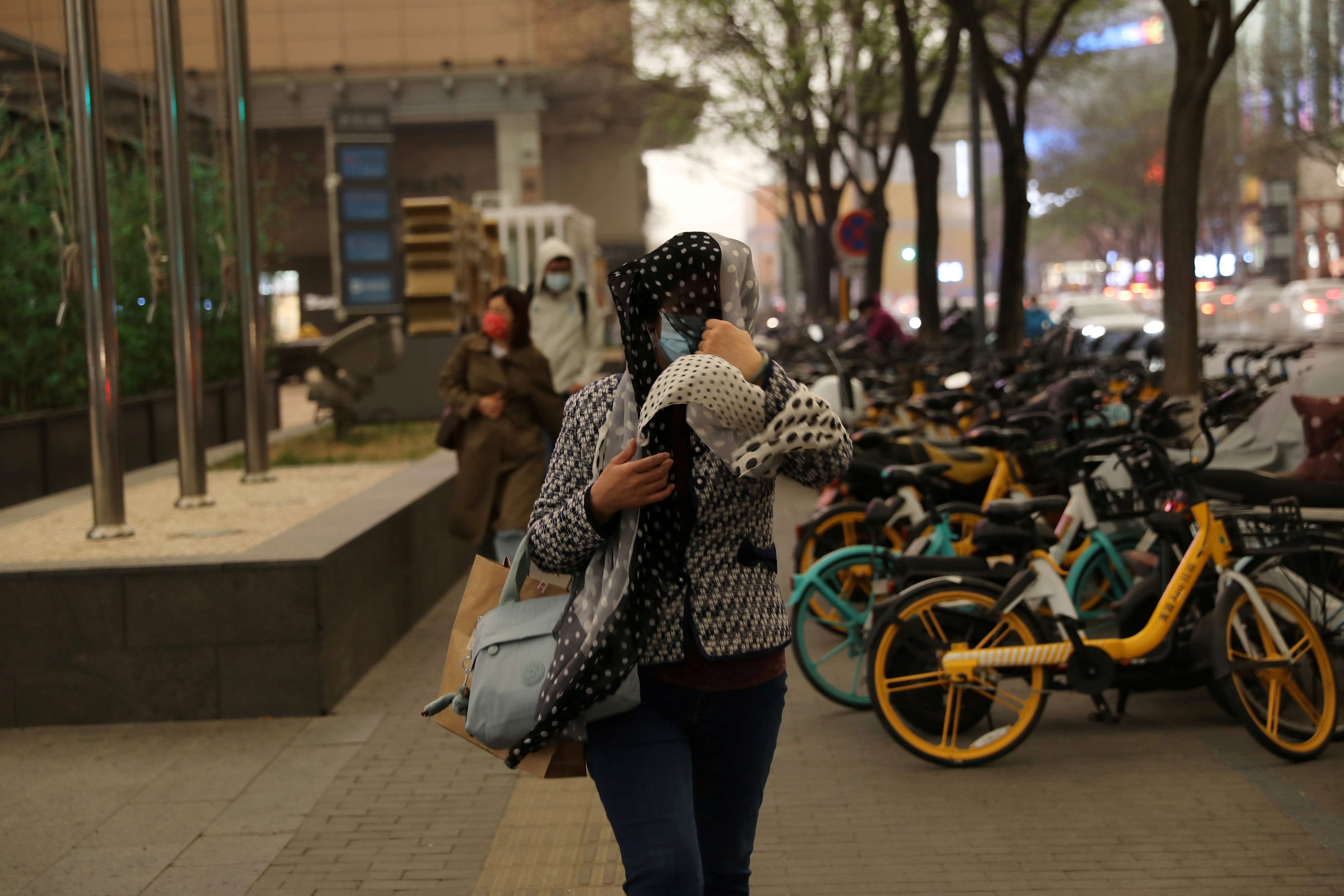 Woman shields herself from wind and rain amid a duststorm in Beijing