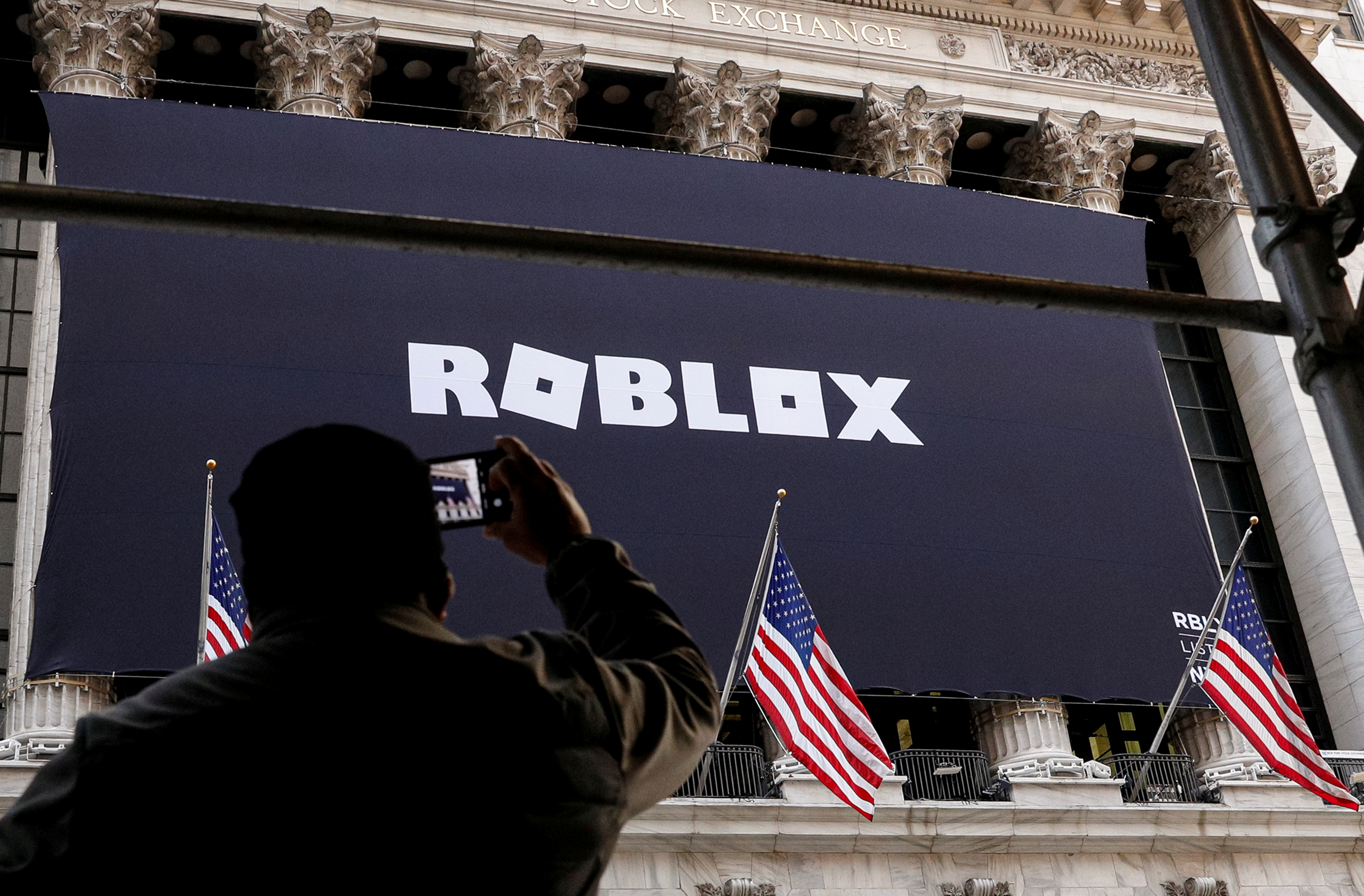 A man photographs a Roblox banner displayed, to celebrate the company's IPO at the NYSE is seen in New York