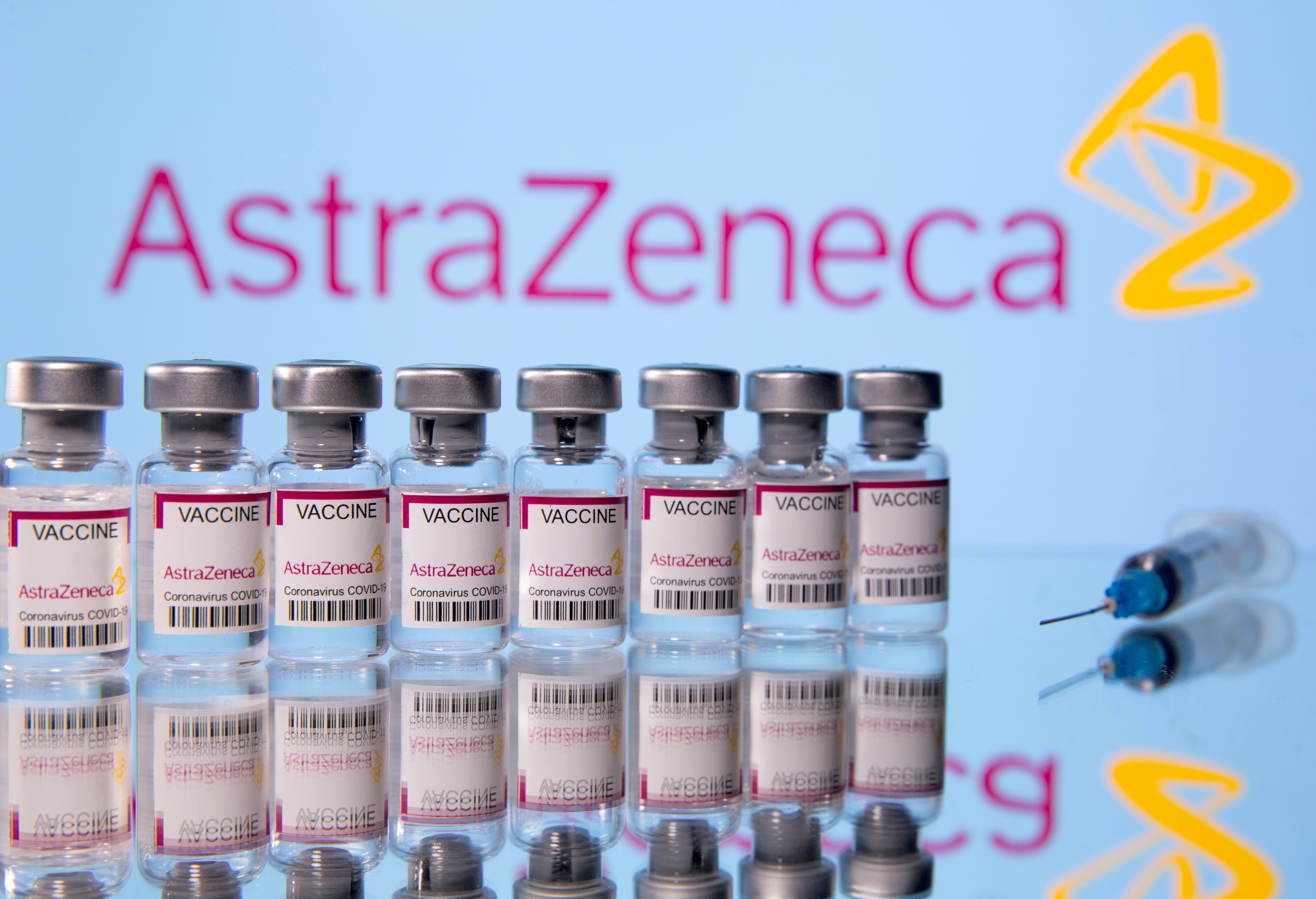 Vials labelled 'Astra Zeneca COVID-19 Coronavirus Vaccine' and a syringe are seen in front of a displayed AstraZeneca logo in this illustration photo