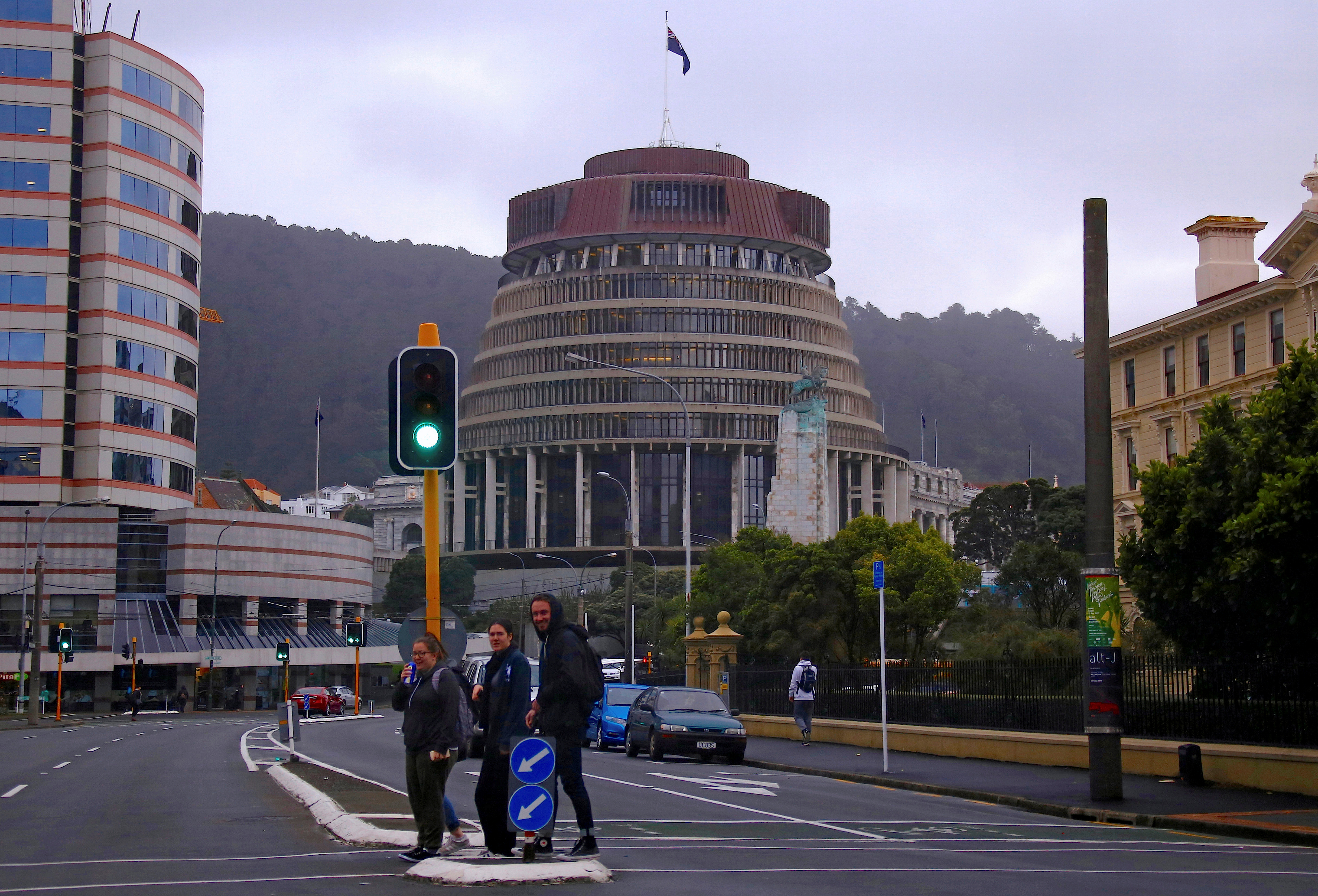 Pedestrians walk across a road in front of the New Zealand parliament building