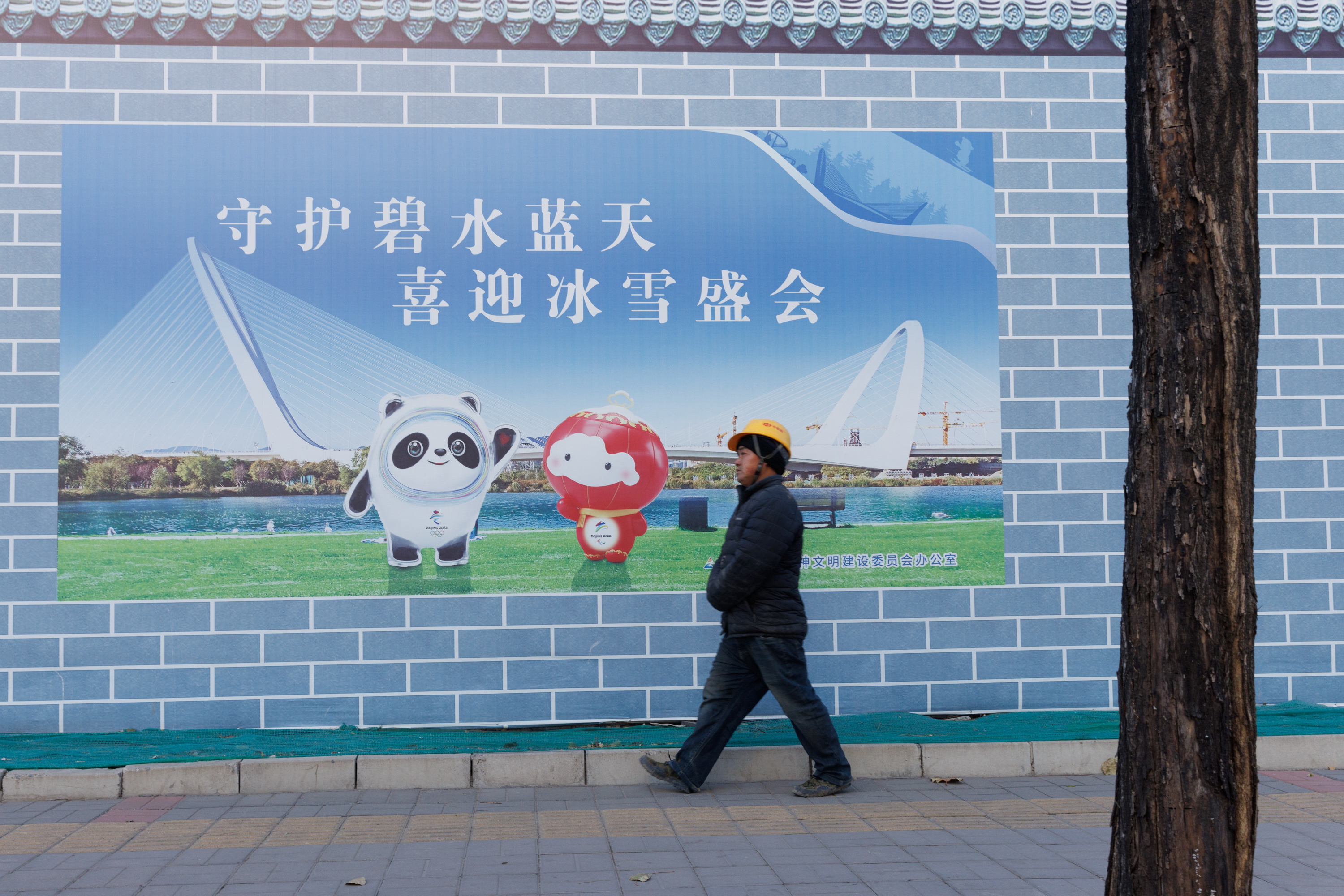 A worker walks past a poster showing the mascots of the Beijing 2022 Olympic and Paralympic Winter Games in Beijing