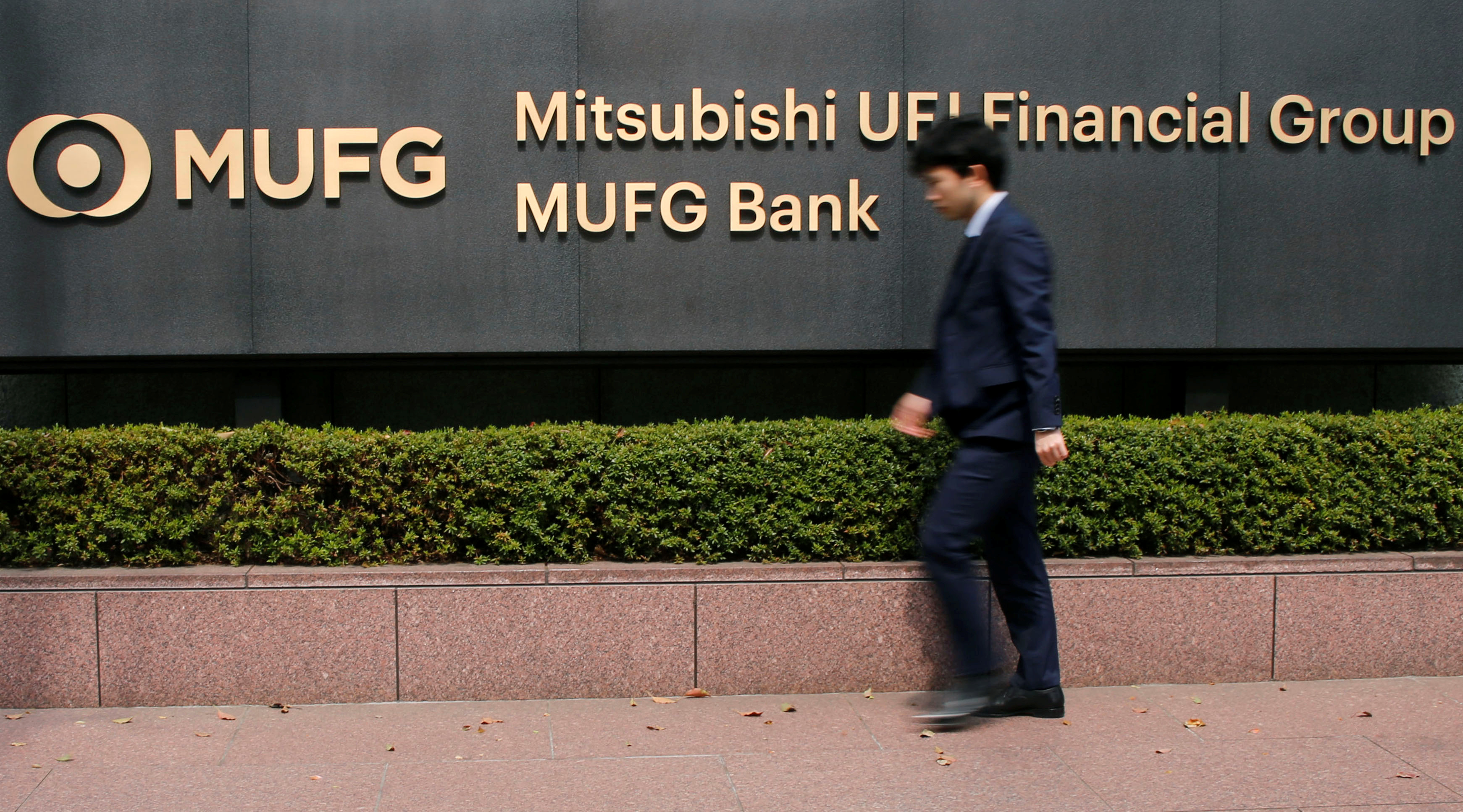 A man walks past a signboard of Mitsubishi UFJ Financial Group and MUFG Bank at its headquarters in Tokyo