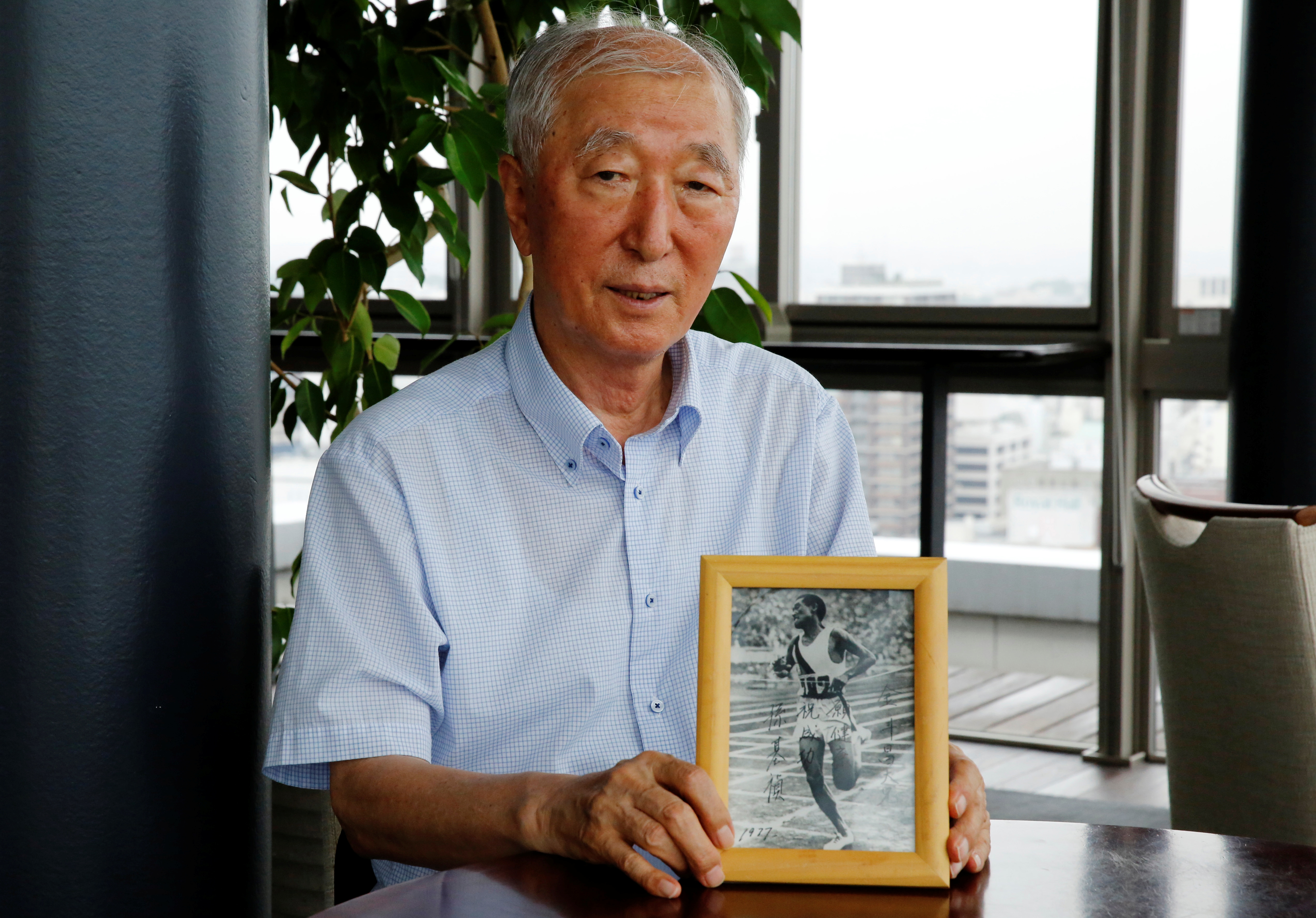 Son Chung-in poses with a photograph of his father, Sohn Kee-chung, who won the 1936 Berlin Olympics marathon event, during an interview with Reuters in Yokohama