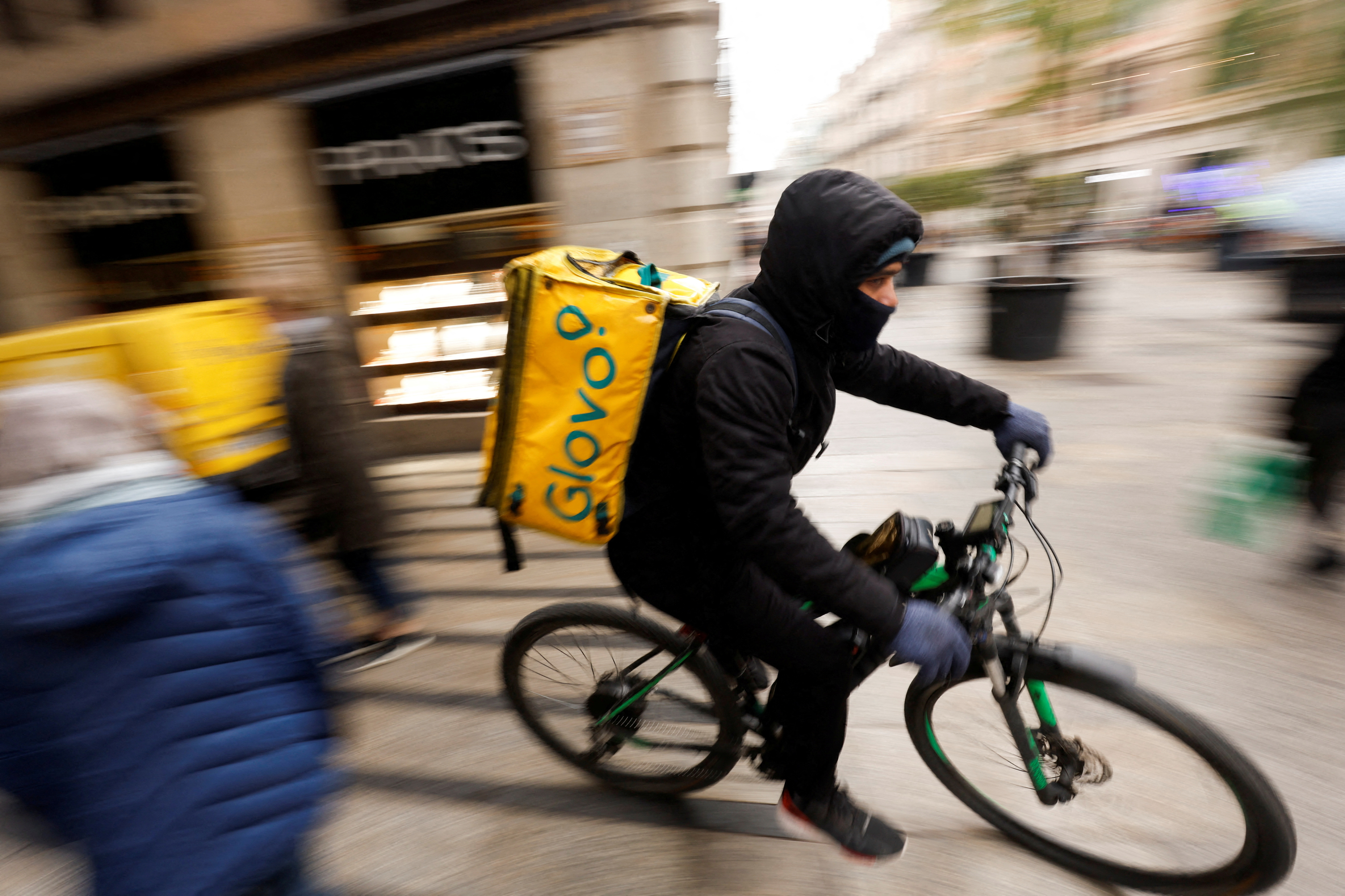 A Glovo delivery rider passes by a pedestrian area in Barcelona