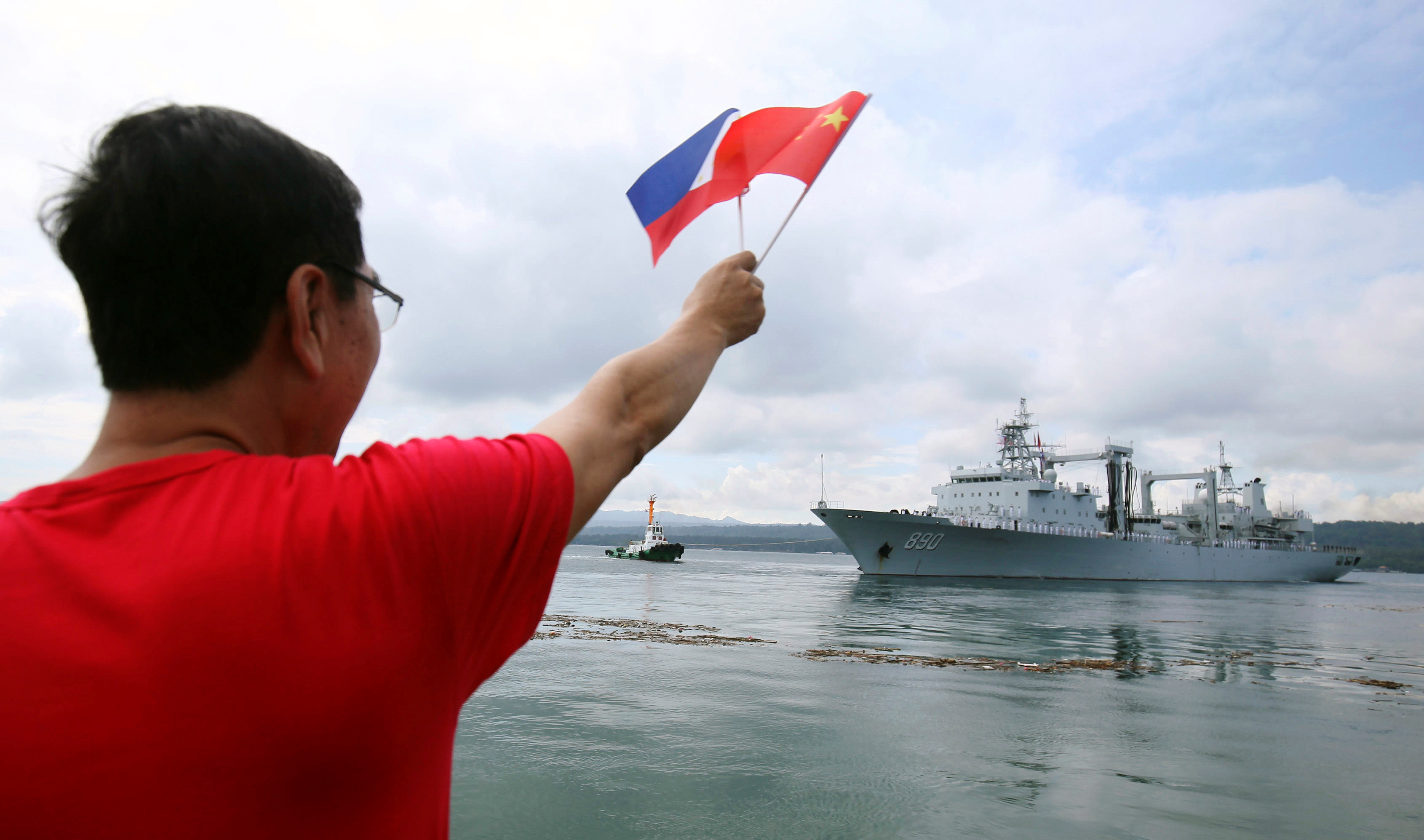 A resident waves miniature Philippine-Chinese flags as a Chinese naval ship departs after a visit in Davao
