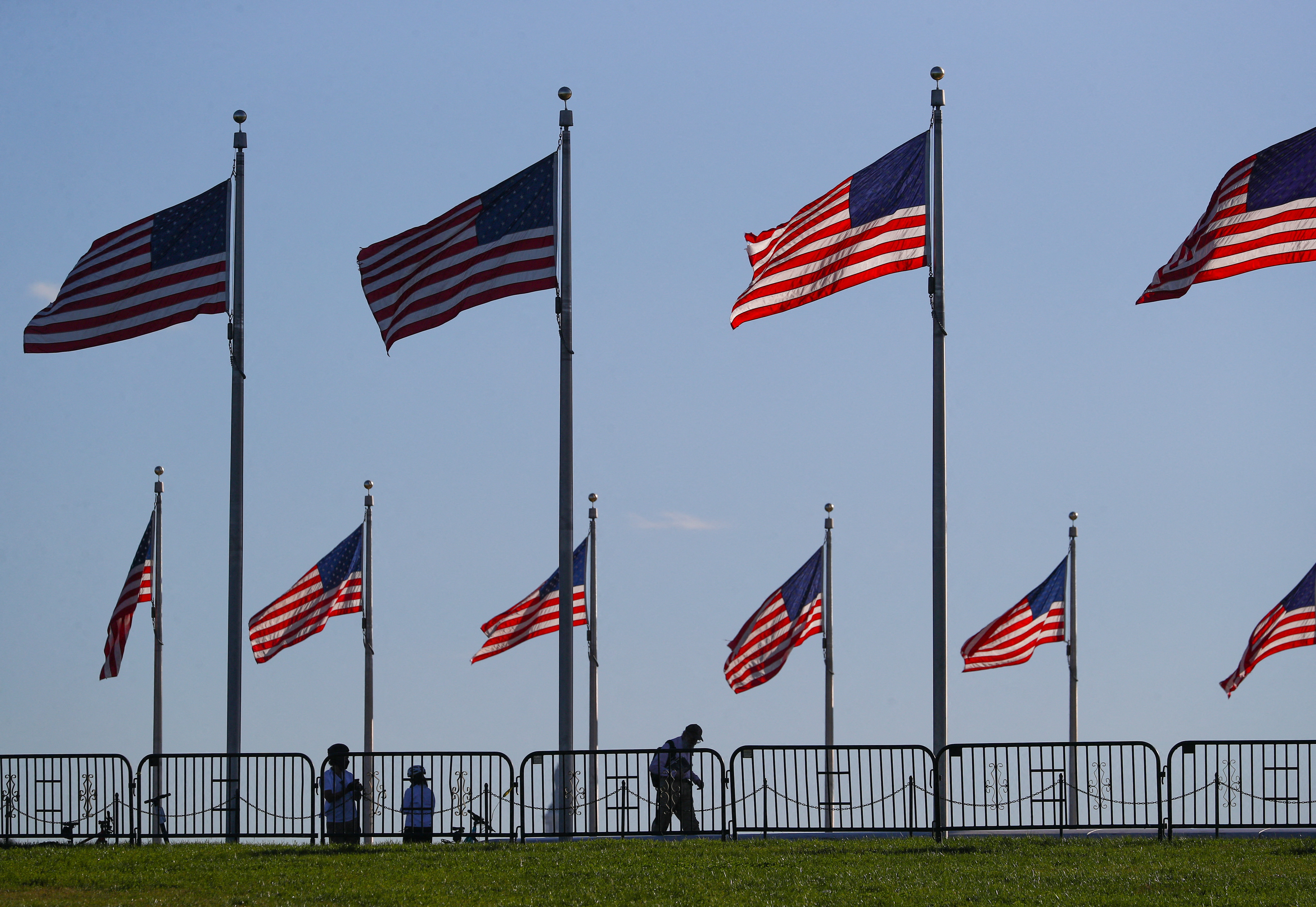 People walk beneath U.S. flags surrounding the Washington monument on the National mall, near the White House in Washington