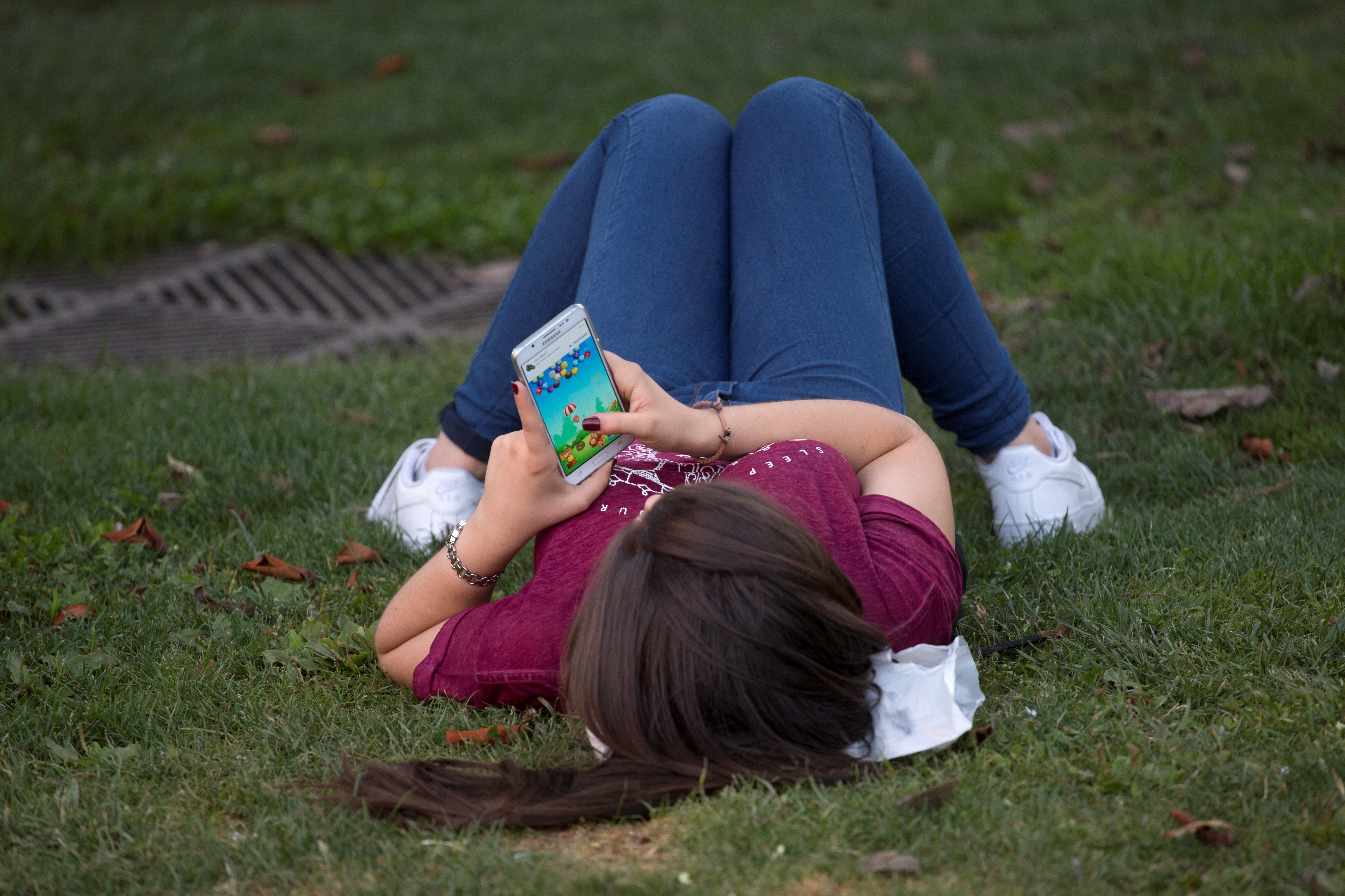 A woman plays a game on her cell phone while lying on the grass in Madrid