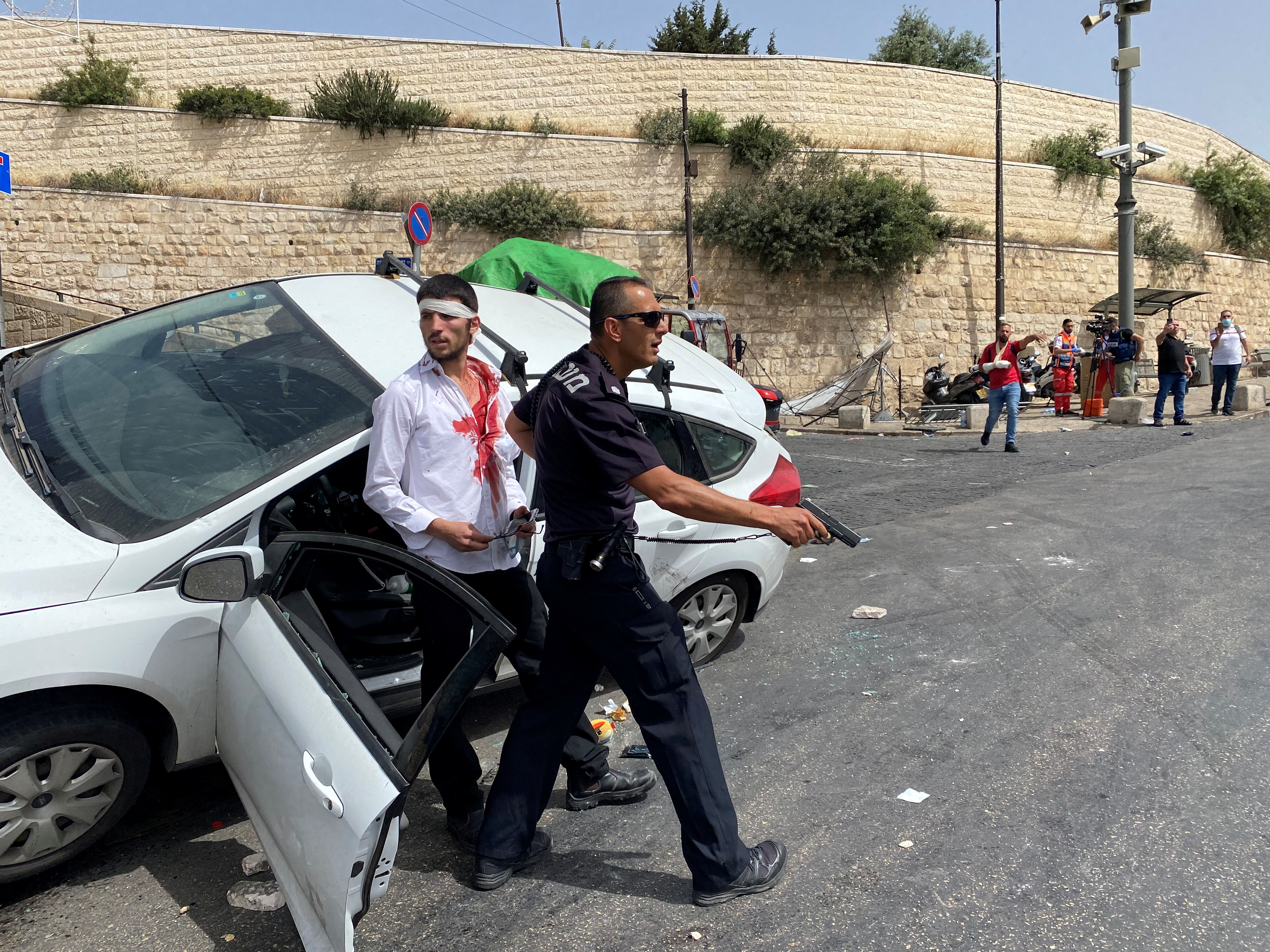 An Israeli policeman holds his weapon as he stands in front of an injured Israeli driver moments after witnesses said his car crashed into a Palestinian on a pavement during stone-throwing clashes near Lion's Gate just outside Jerusalem's Old City