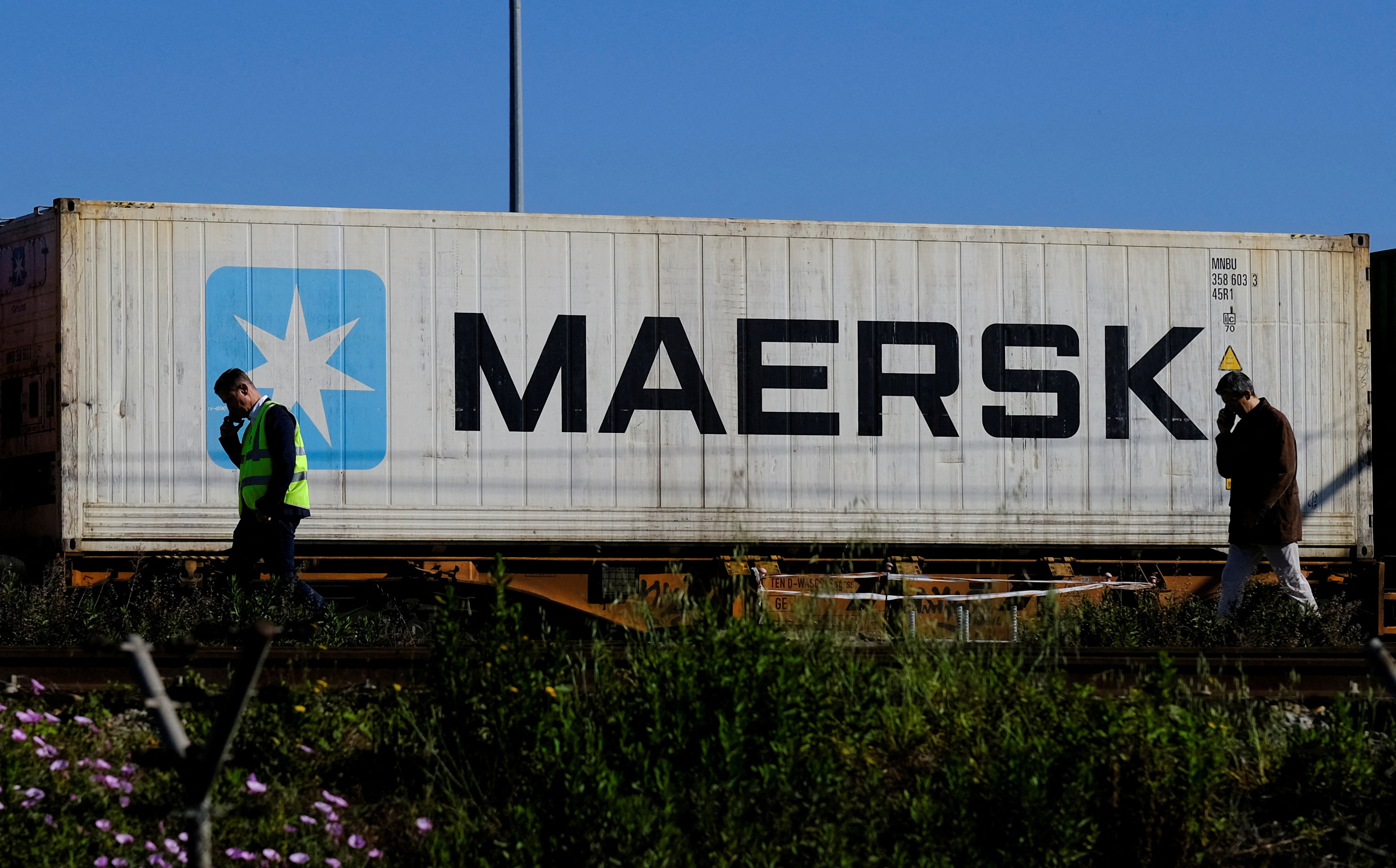 Workers talk on their mobile phones as a Maersk container is transported by a train near a port of Barcelona