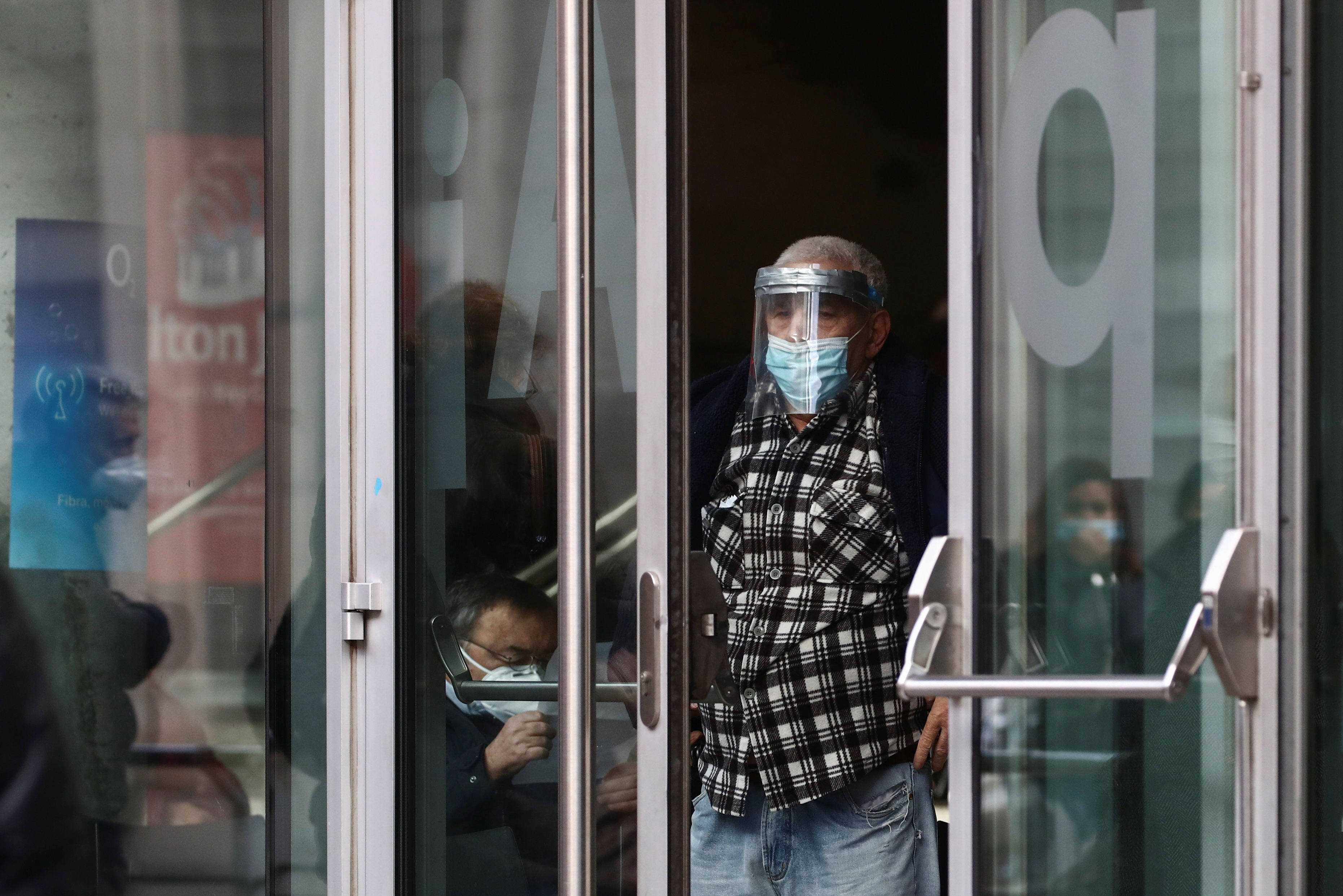 A man wearing a protective face shield and a mask stands at an entrance, after getting his dose of coronavirus disease (COVID-19) vaccine at a vaccination centre in Madrid, Spain, November 24, 2021. REUTERS/Sergio Perez