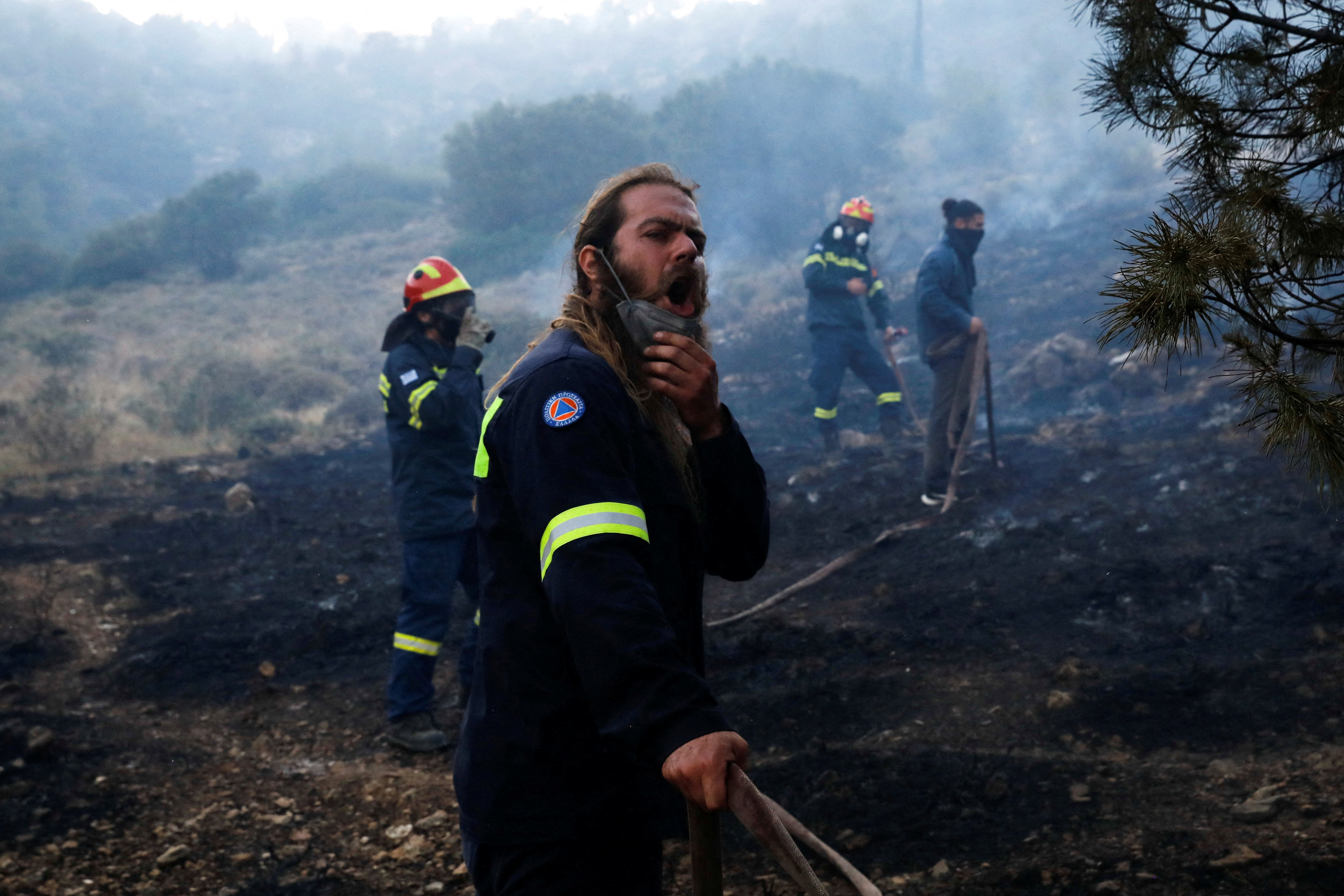 A volunteer holds a hose as a wildfire burning near Vari, south of Athens
