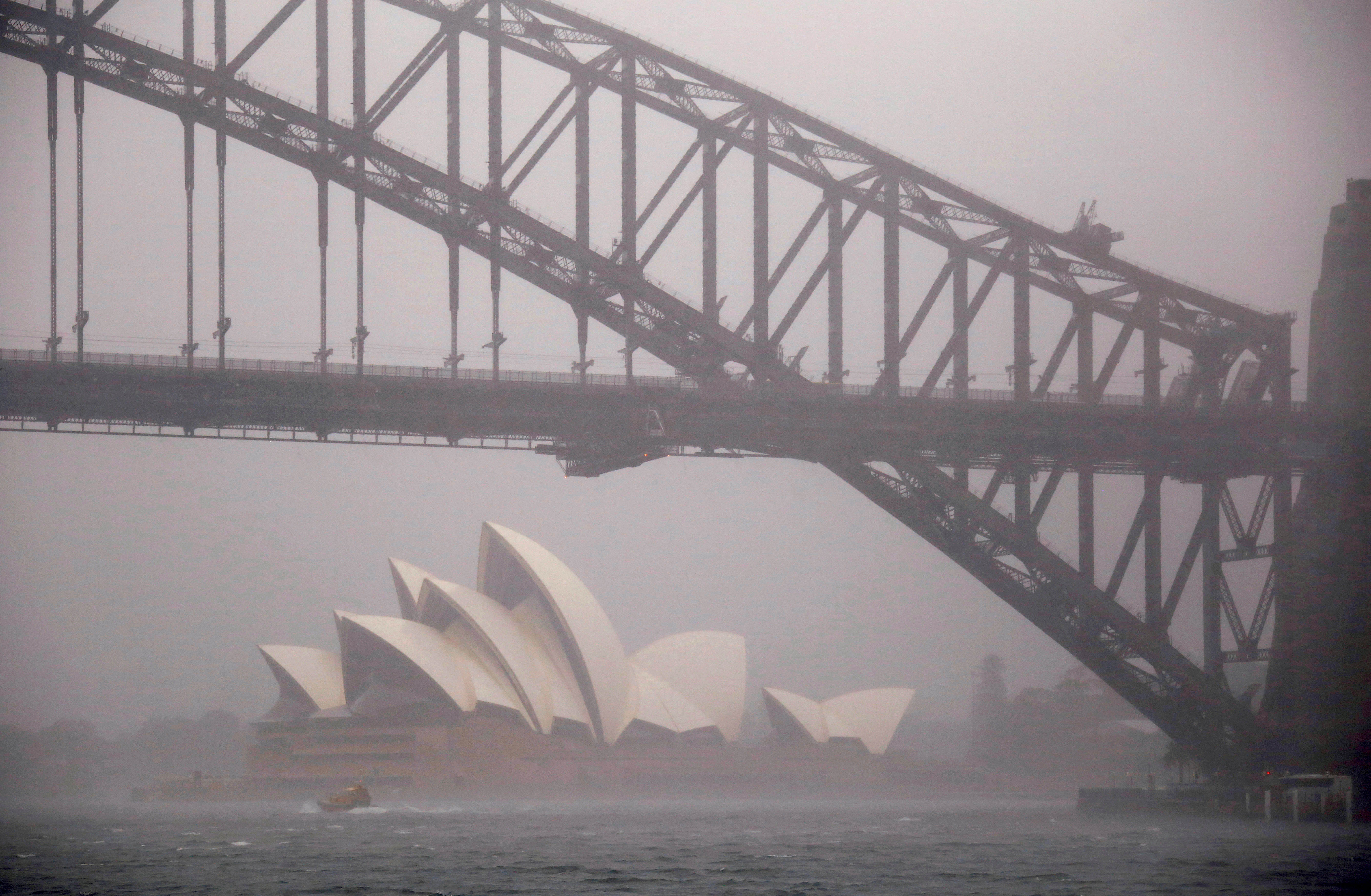 A boat passes under the Sydney Harbour Bridge and in front of the Sydney Opera House as strong winds and heavy rain hit the city of Sydney