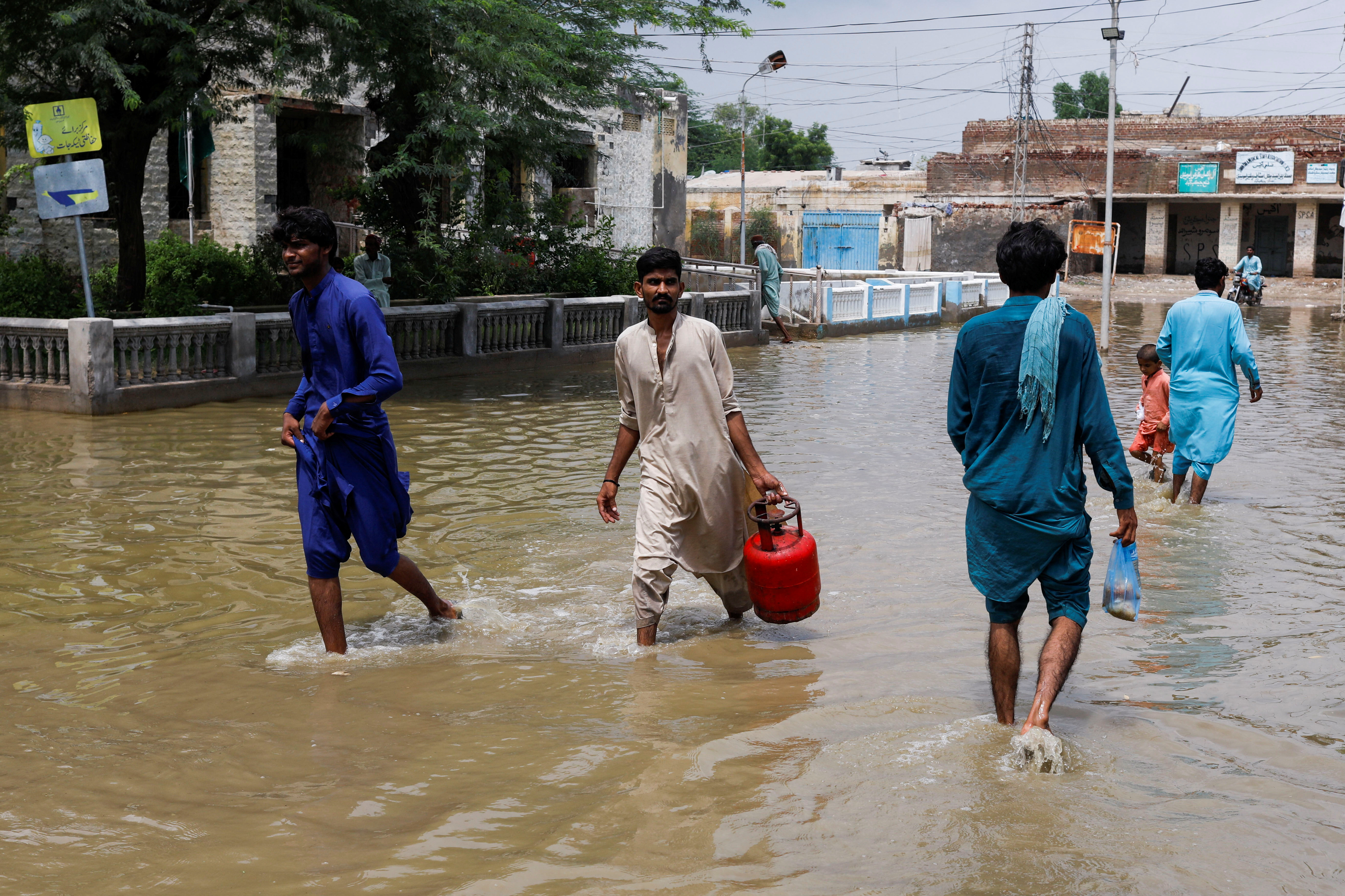 Men walk through rain waters, following rains and floods during the monsoon season in Jacobabad