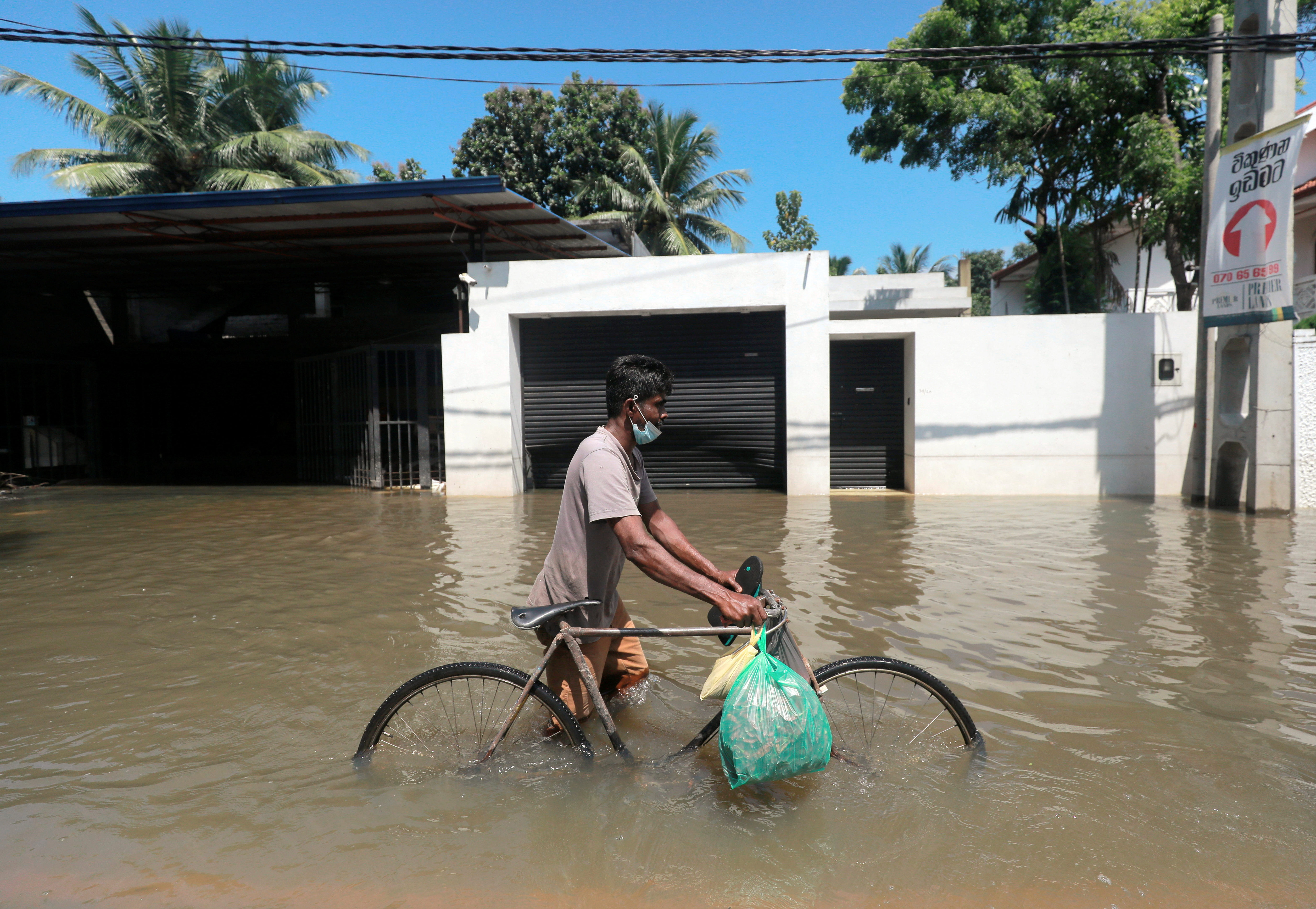 A man pushes a bike along a flooded road after a heavy rainfall in Kochchikade, Sri Lanka November 11, 2021. REUTERS/Dinuka Liyanawatte