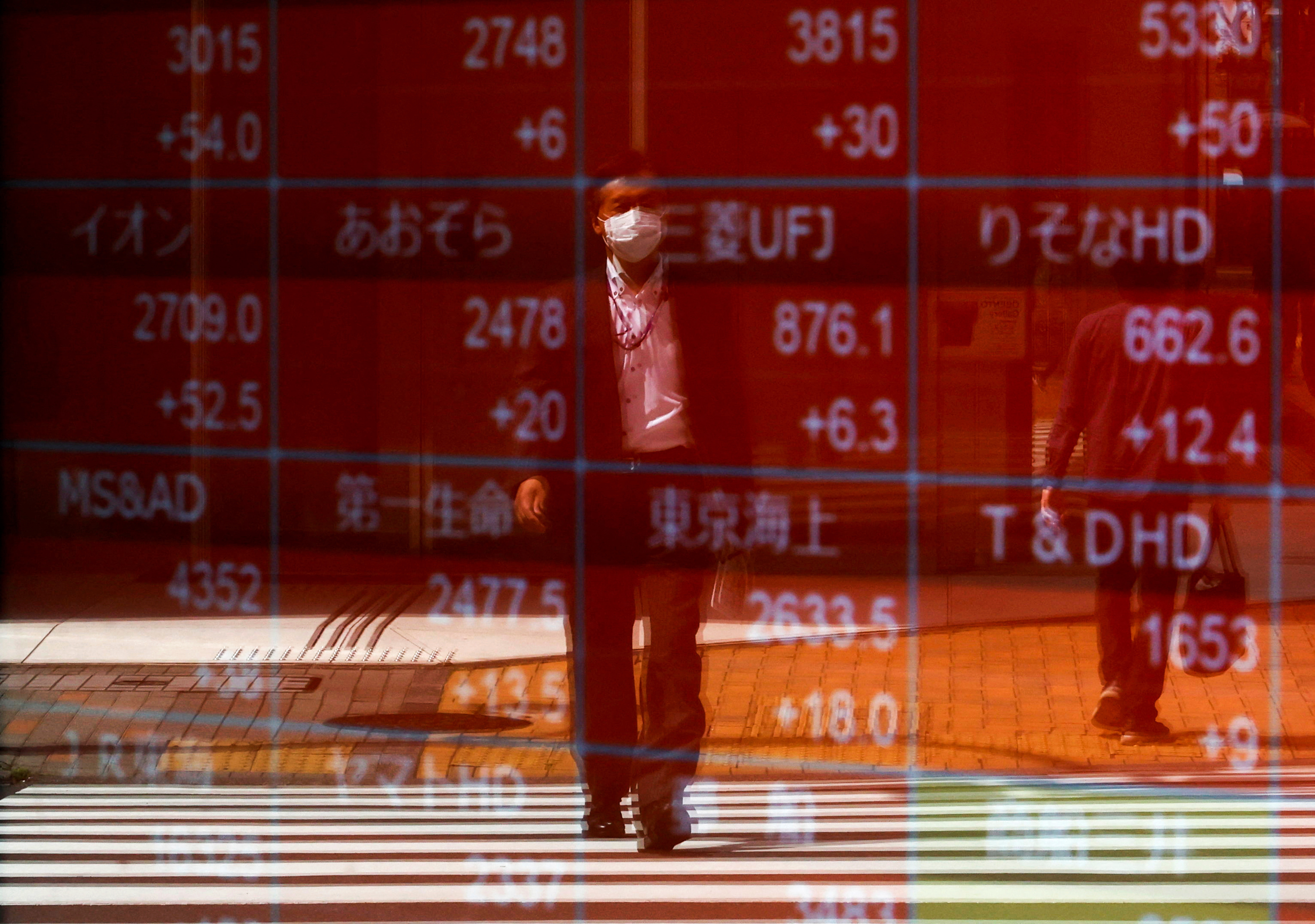 A man is reflected on an electric stock quotation board outside a brokerage in Tokyo