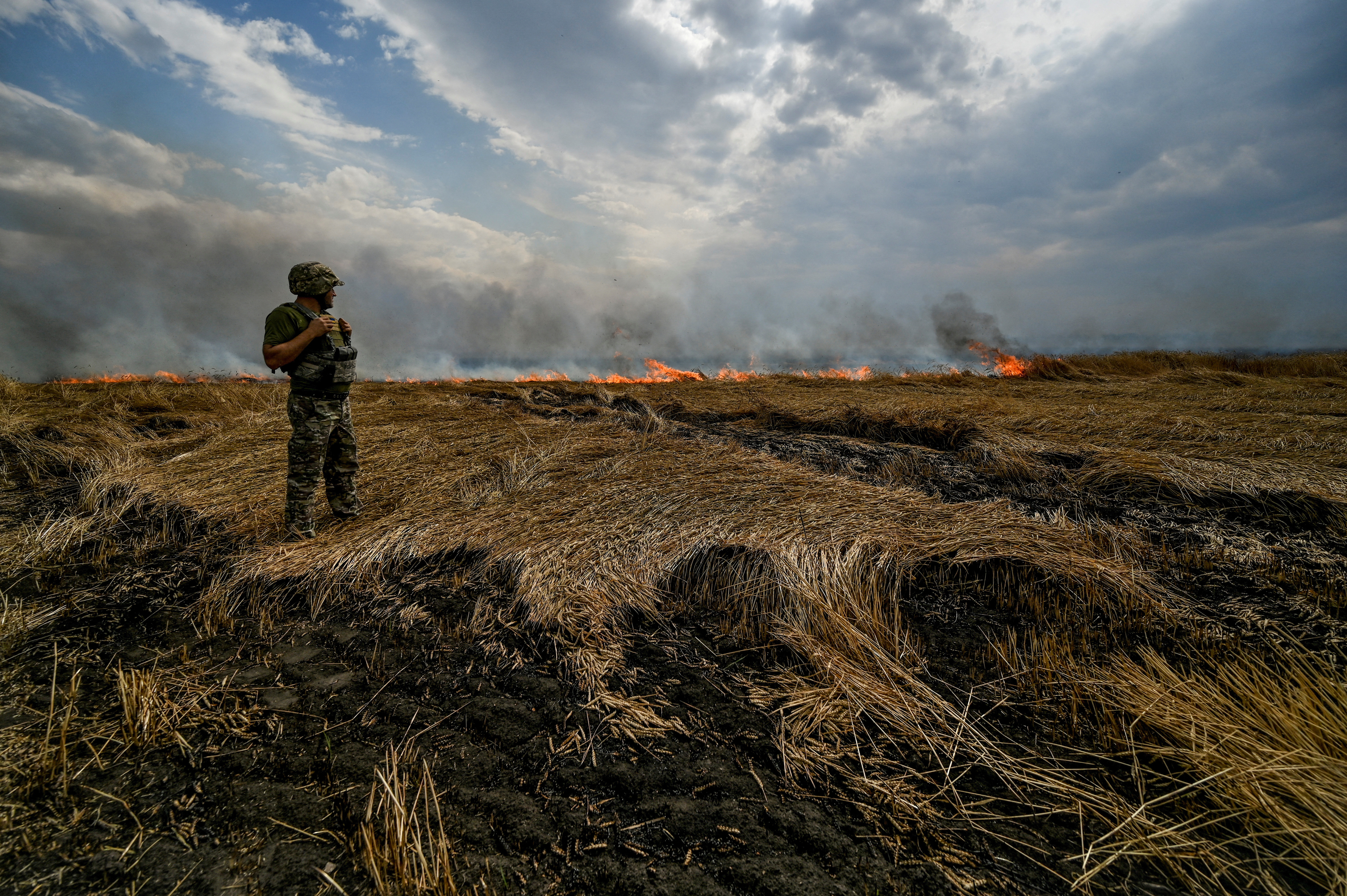 A Ukrainian serviceman stands on a burning wheat field near a frontline on a border between Zaporizhzhia and Donetsk regions