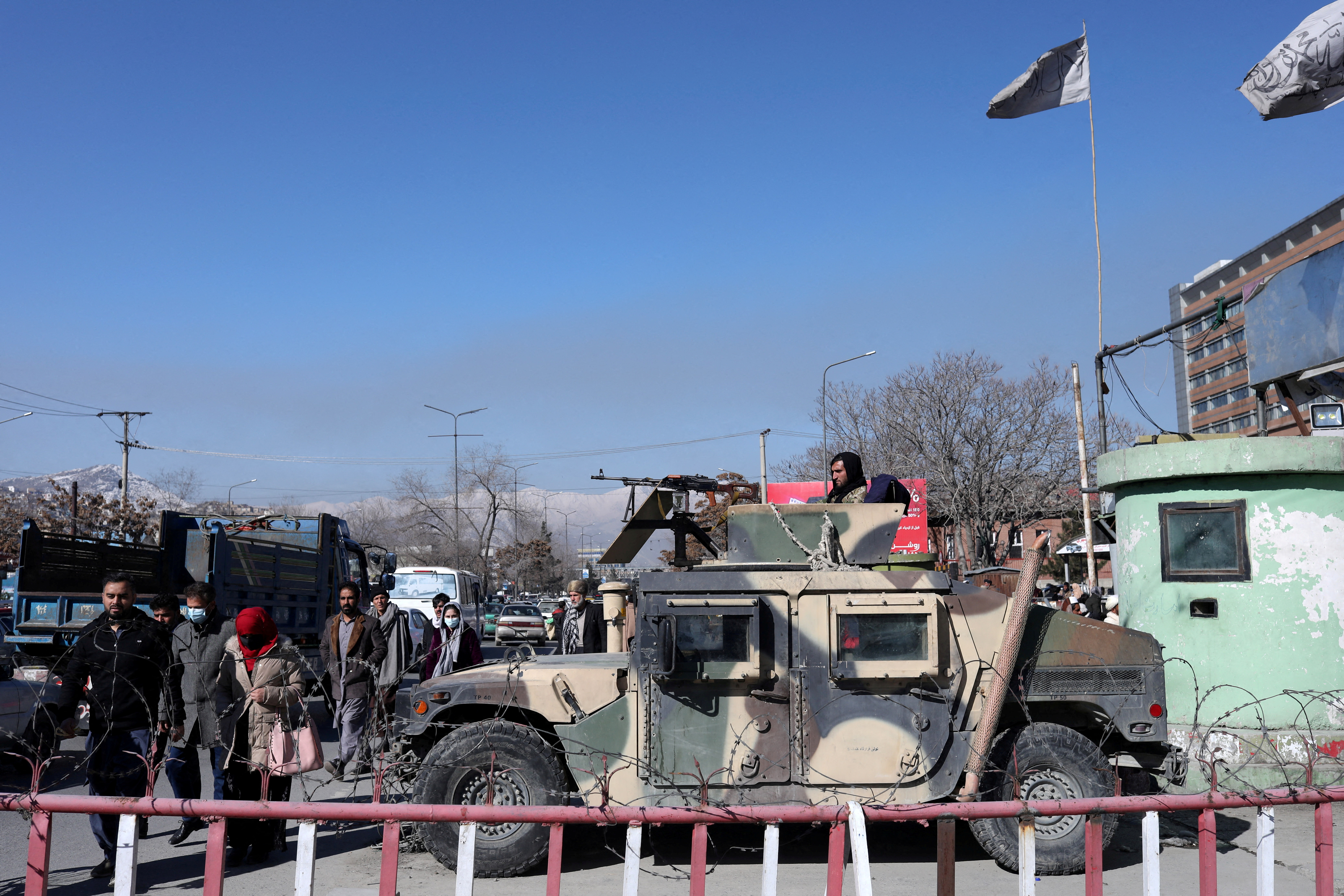 Afghans walk past a Humvee with a Taliban fighter on it guarding the road in Kabul