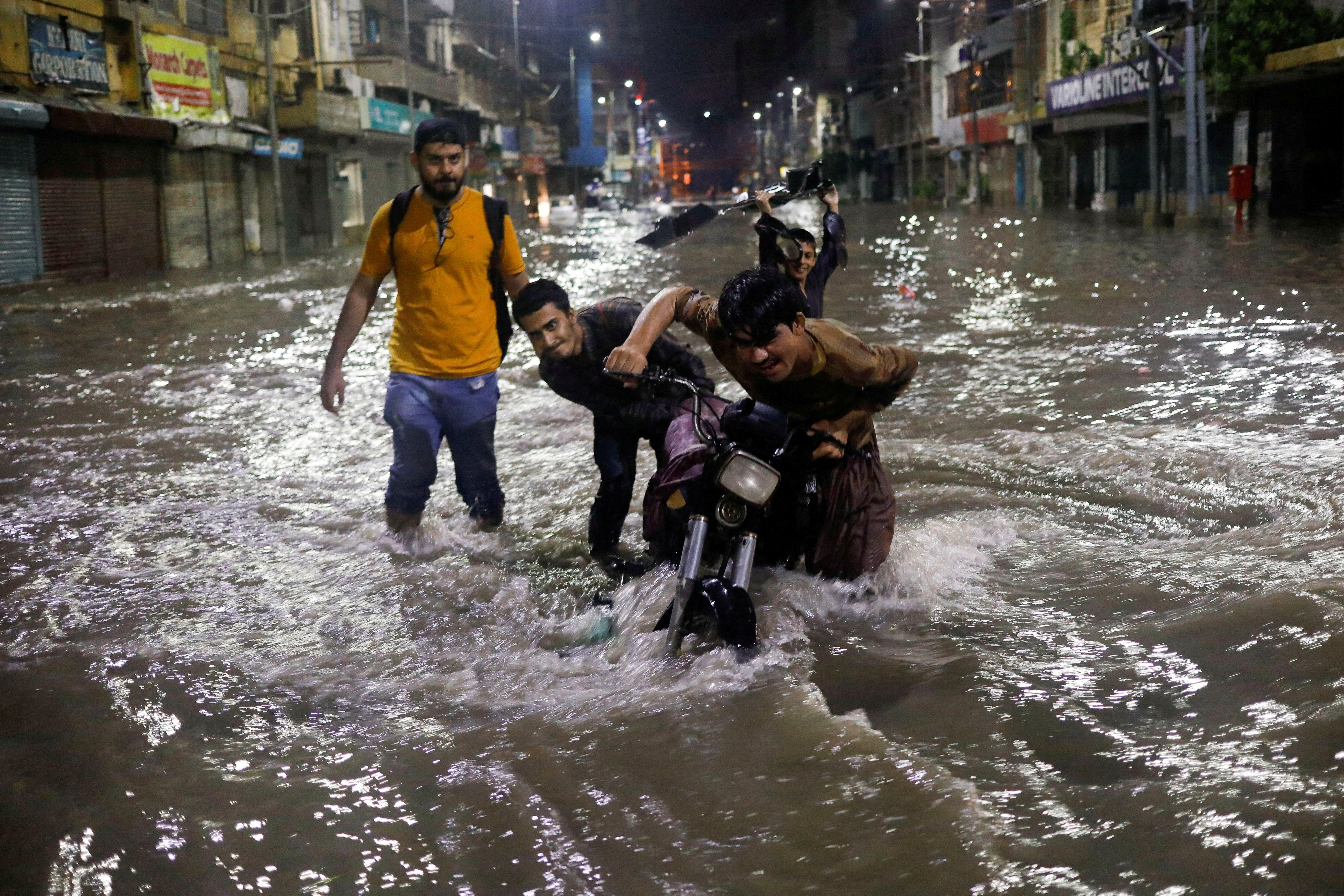 Boys push their motorcycle after it was stopped on a flooded street, following heavy rains during the monsoon season in Karachi
