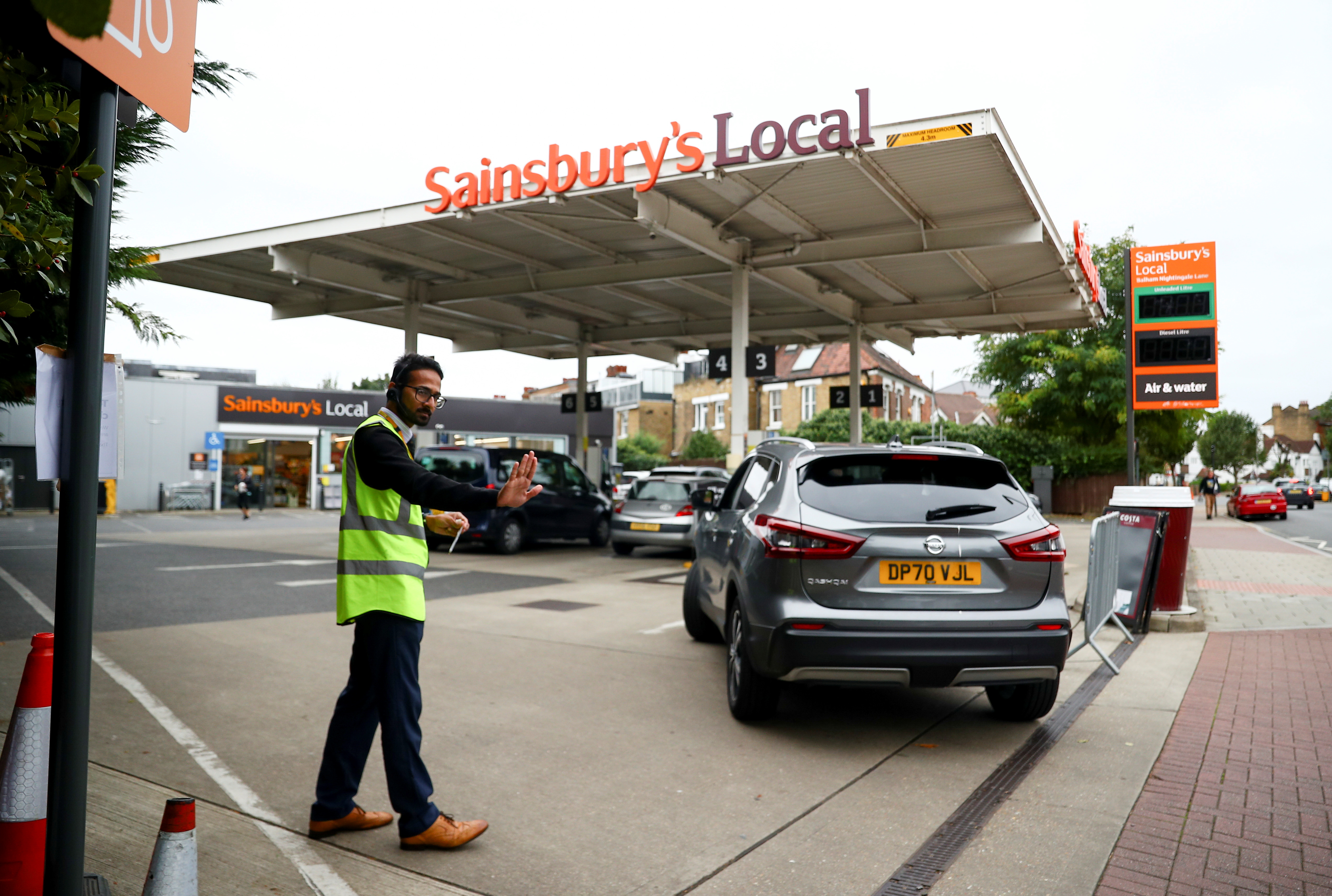 A worker guides vehicles into the forecourt as they queue to refill at a fuel station in London