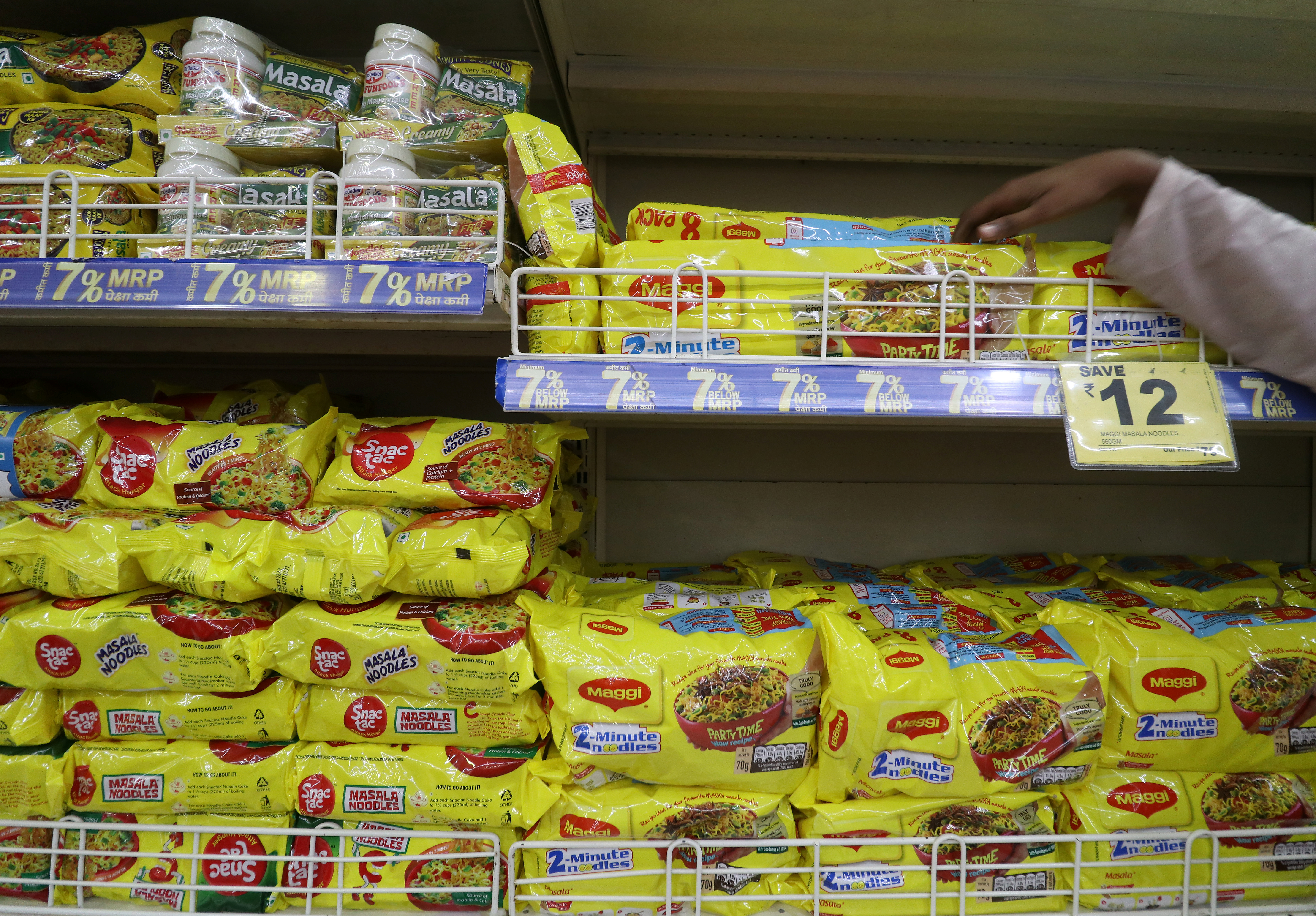 A worker arranges packets of Nestle's Maggi noodles next to Reliance's Snac tac noodles on a shelf inside a Reliance supermarket in Mumbai