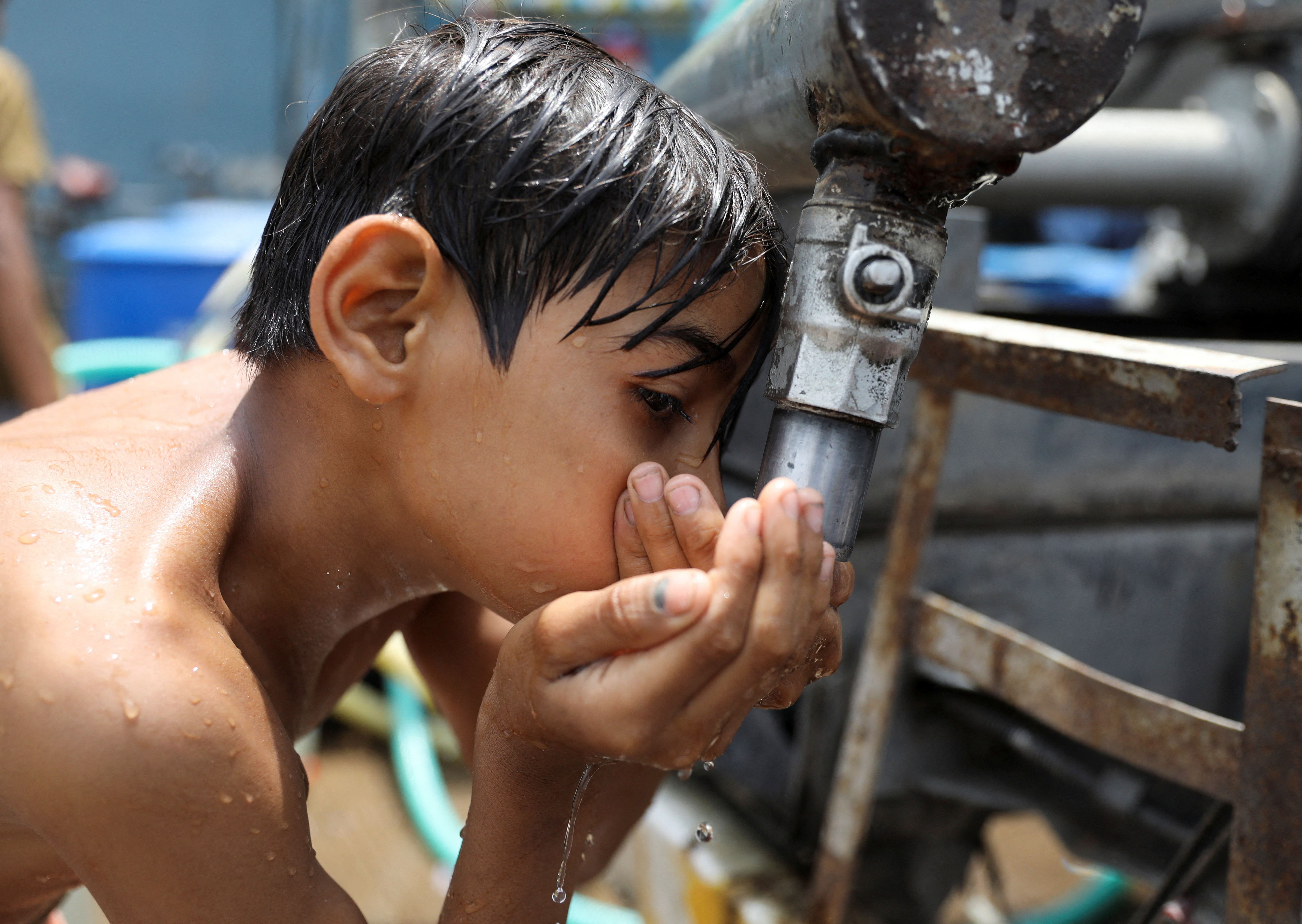 Boy drinks water from a municipal tanker on a hot summer day in New Delhi