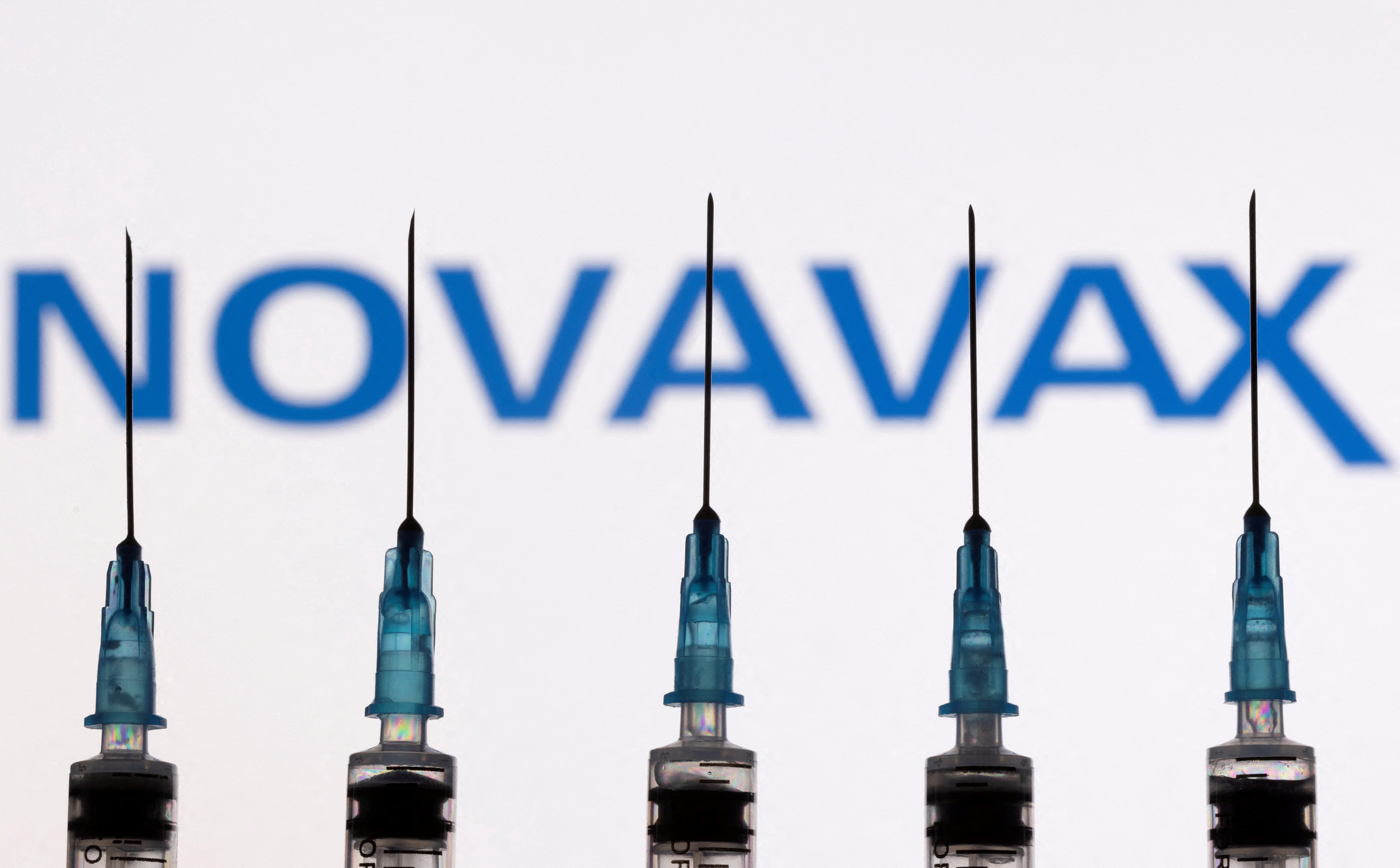 Syringes with needles are seen in front of a displayed Novavax logo in this illustration taken