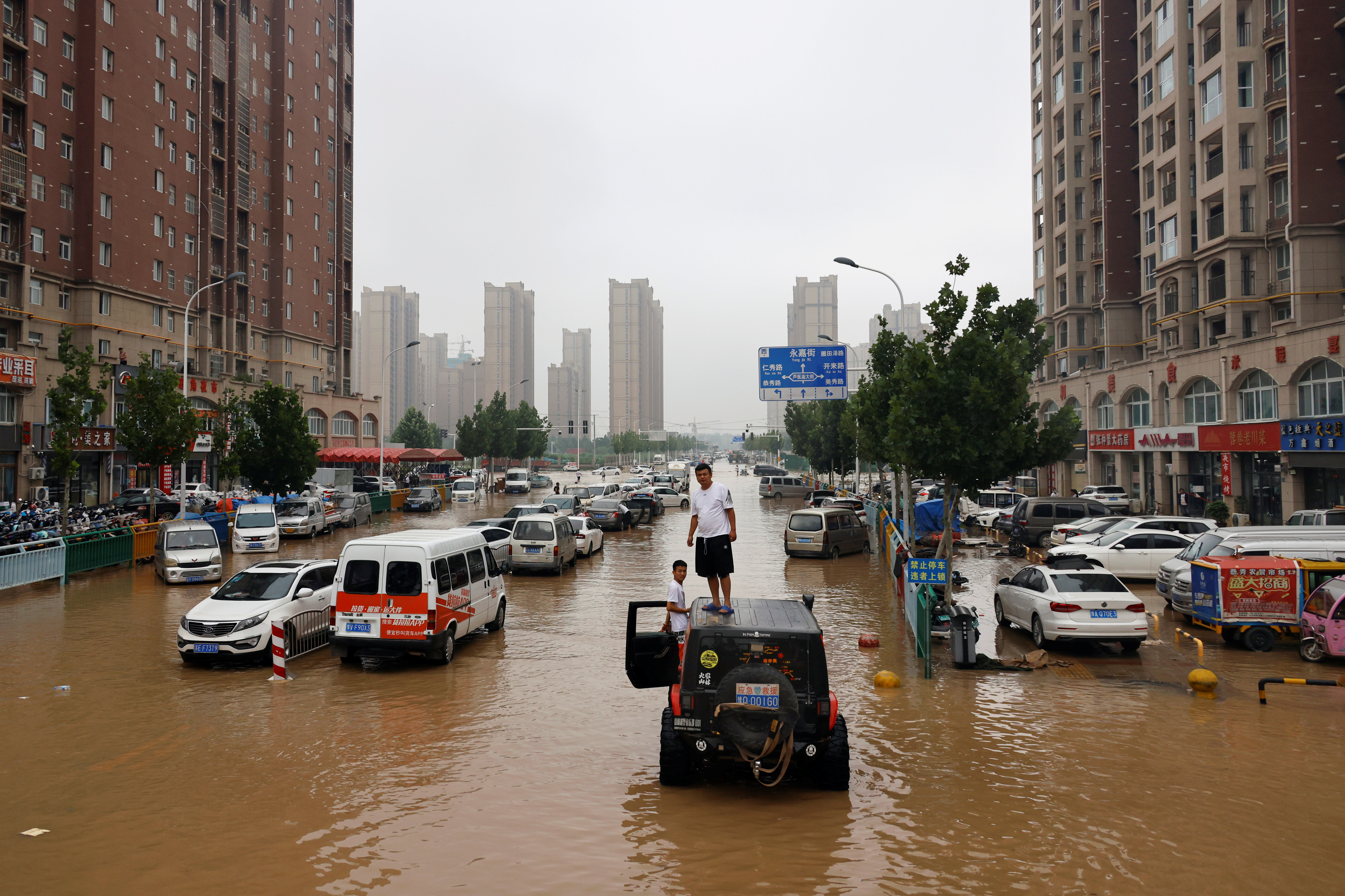Men stand on a vehicle on a flooded road following heavy rainfall in Zhengzhou