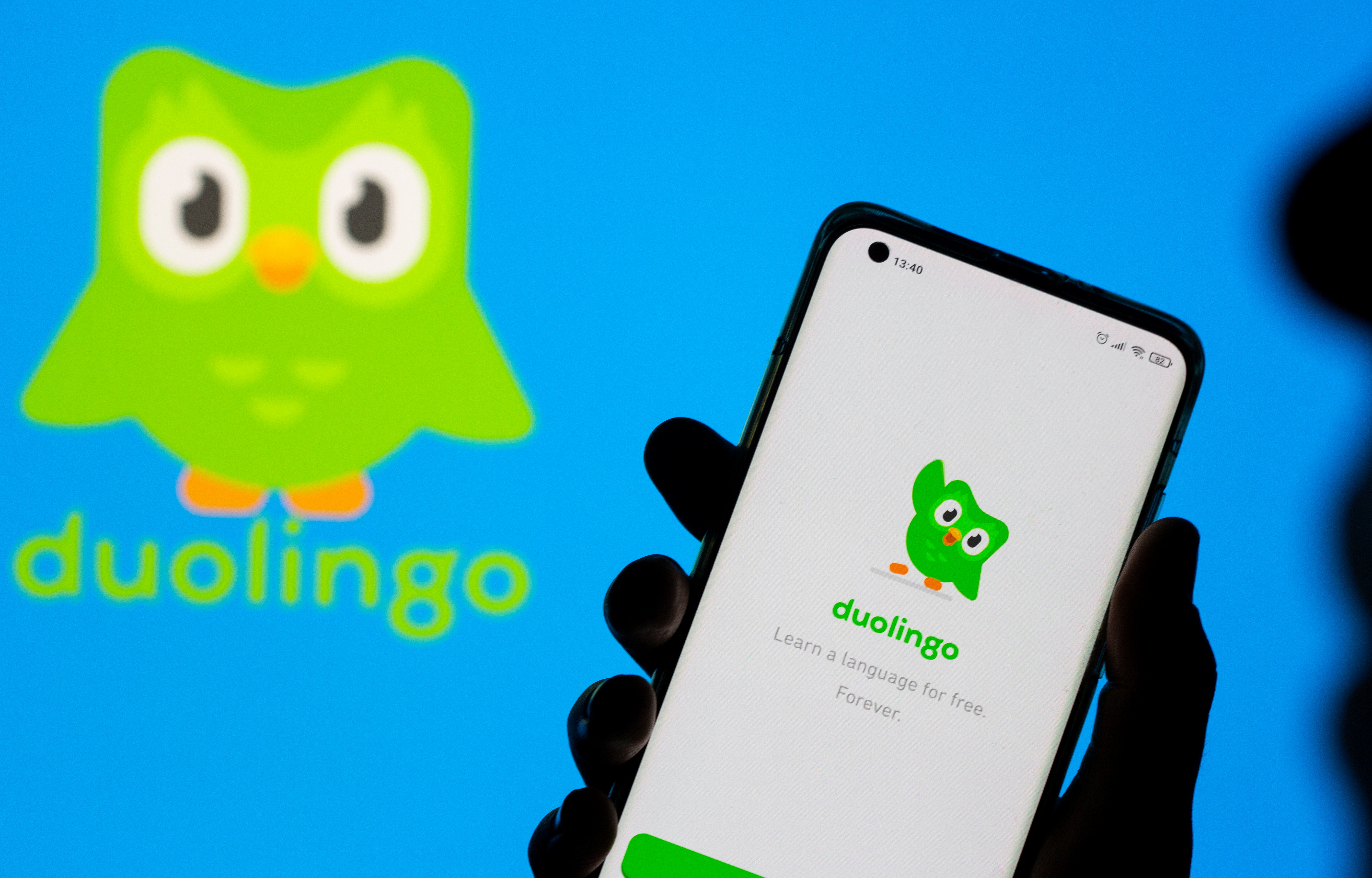 Woman with her smartphone poses in front of displayed Duolingo logo in this illustration taken