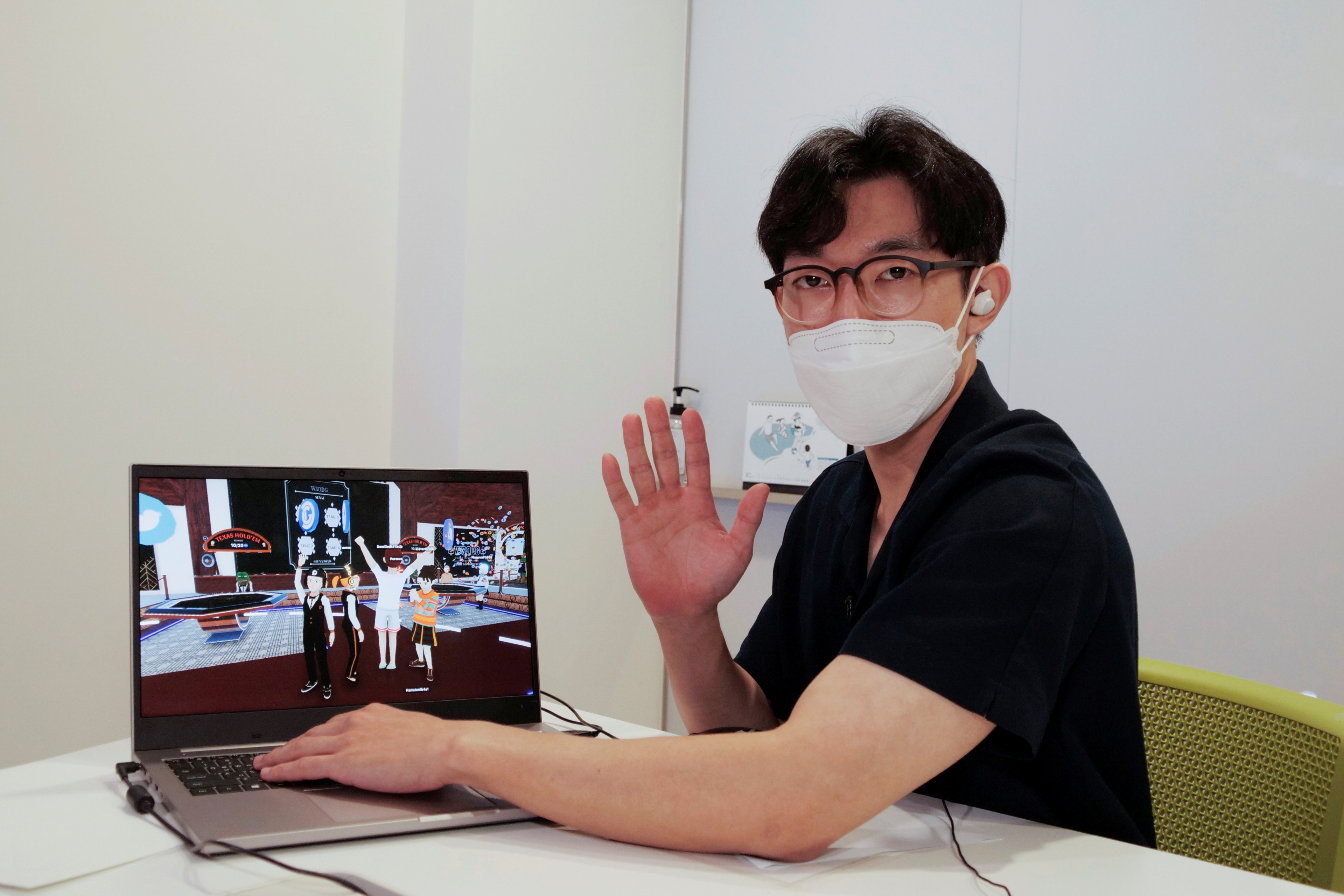 Shaun poses for photographs with a laptop showing his avatar in Decentraland in Seoul