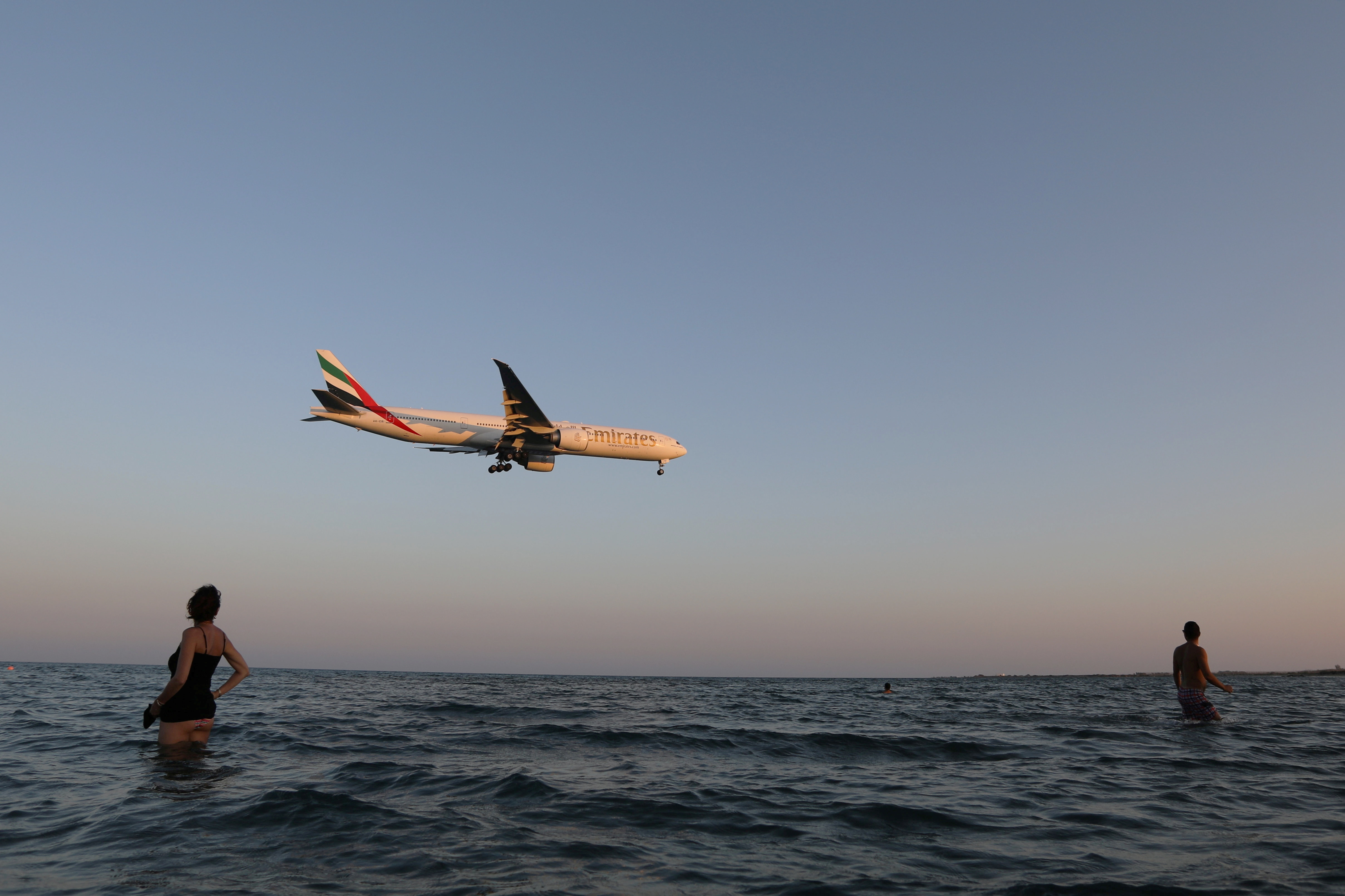 Tourists watch an Emirates Boeing 777 airplane preparing to land at Larnaca International Airport