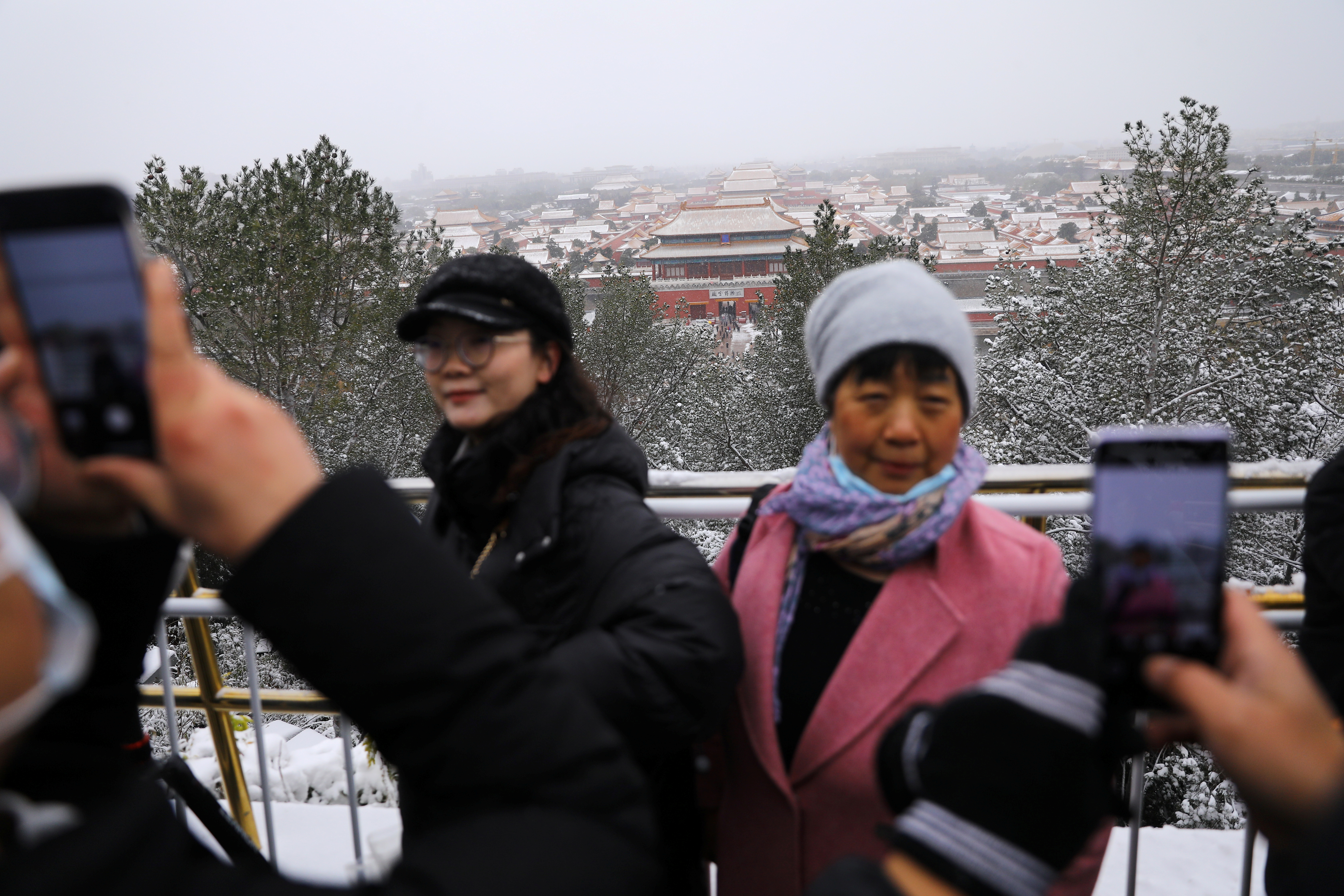 People enjoy snowfall on a peak overlooking the Forbidden City at Jingshan Park, in Beijing