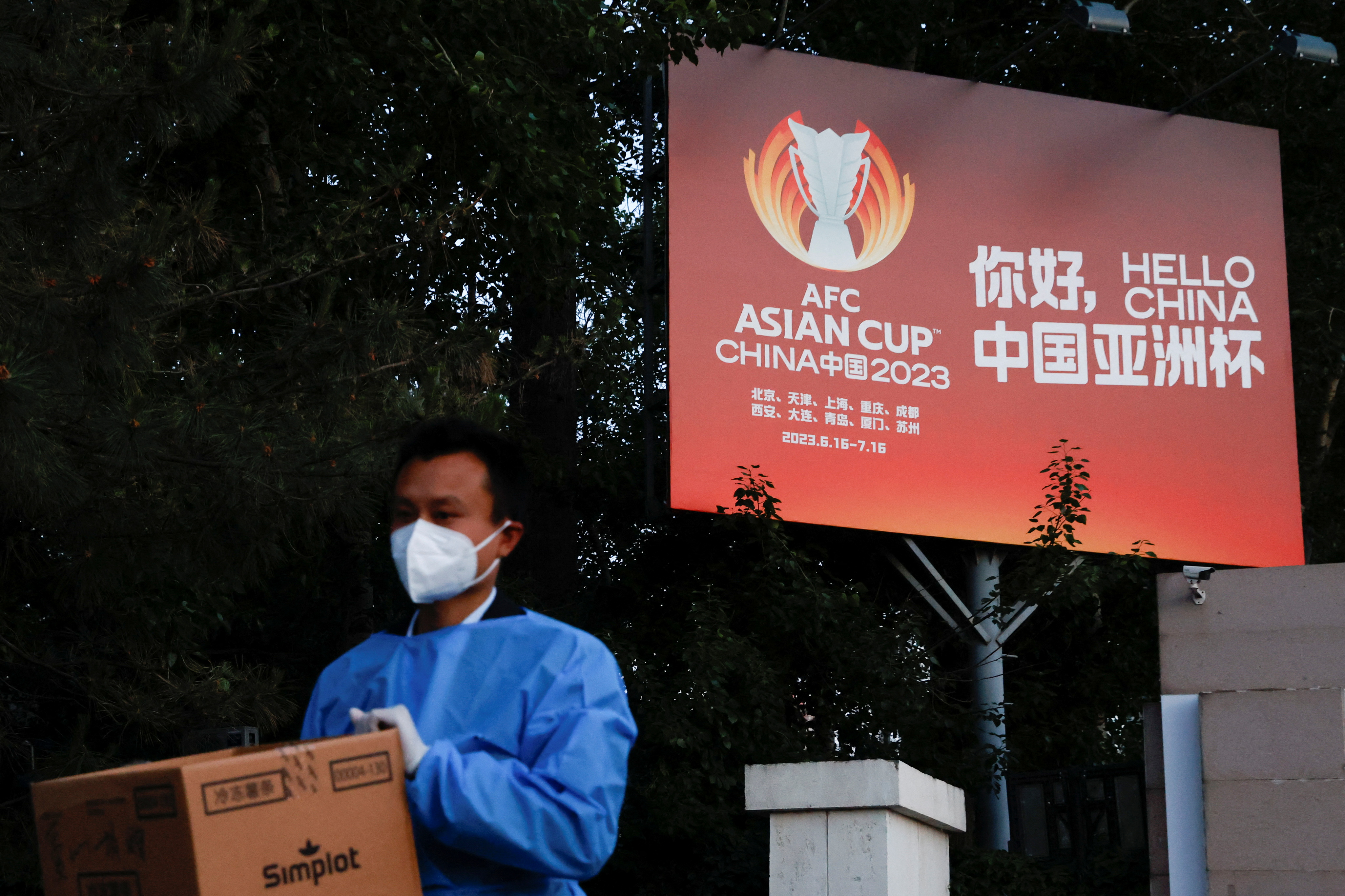 Man wearing PPE walks past a billboard of the AFC Asian Cup, amid the COVID-19 outbreak in Beijing