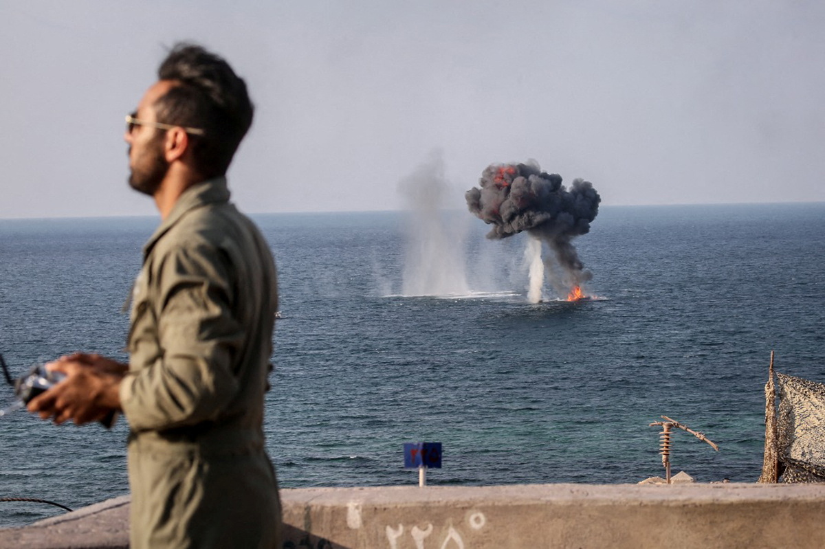 An explosion is seen on the water surface behind a member of the Islamic Revolution Guards Corps (IRGC) during a joint military exercise called the 'Great Prophet 17' in the southwest of Iran