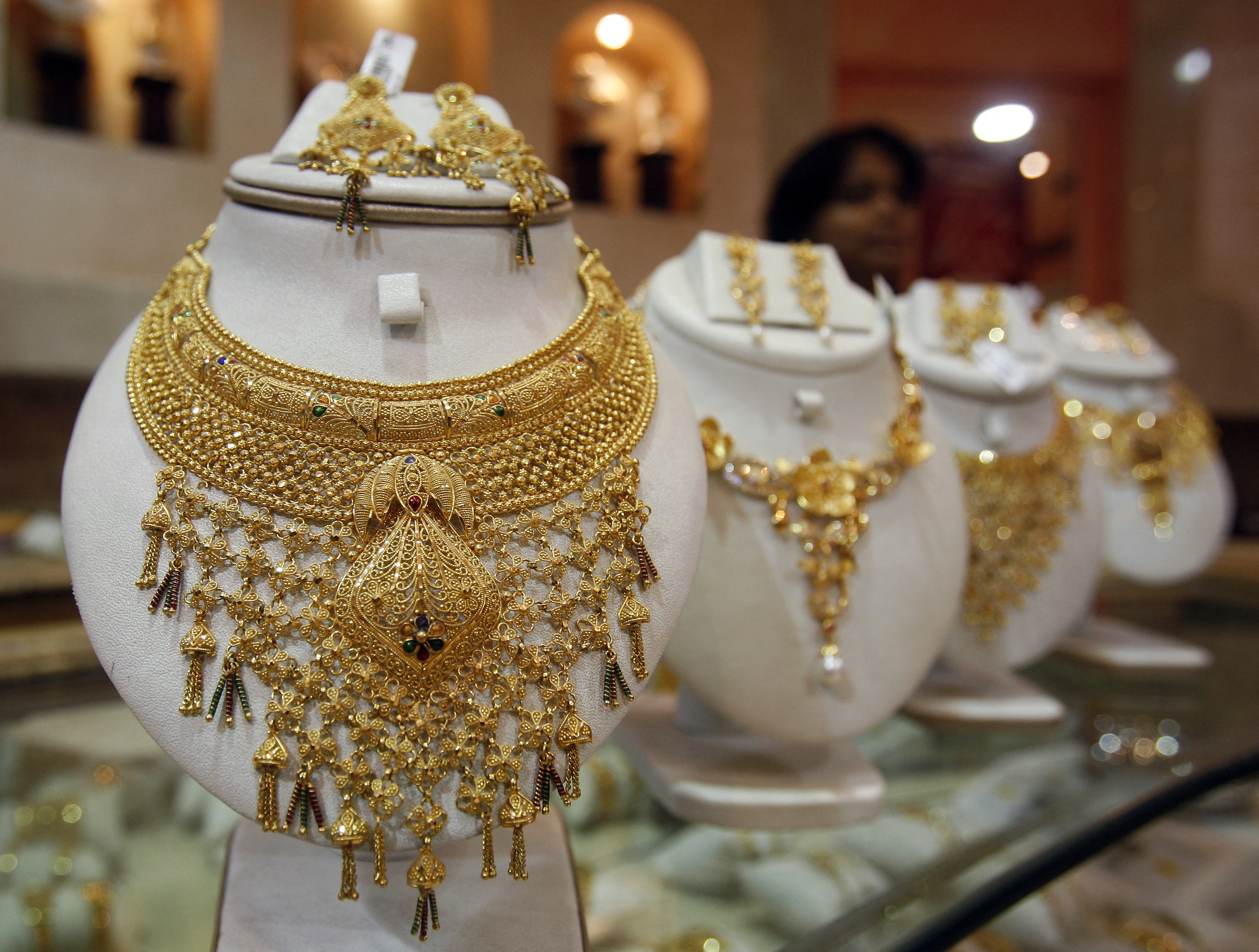 Saleswoman stands behind the showcased gold necklaces at a jewellery showroom in Agartala