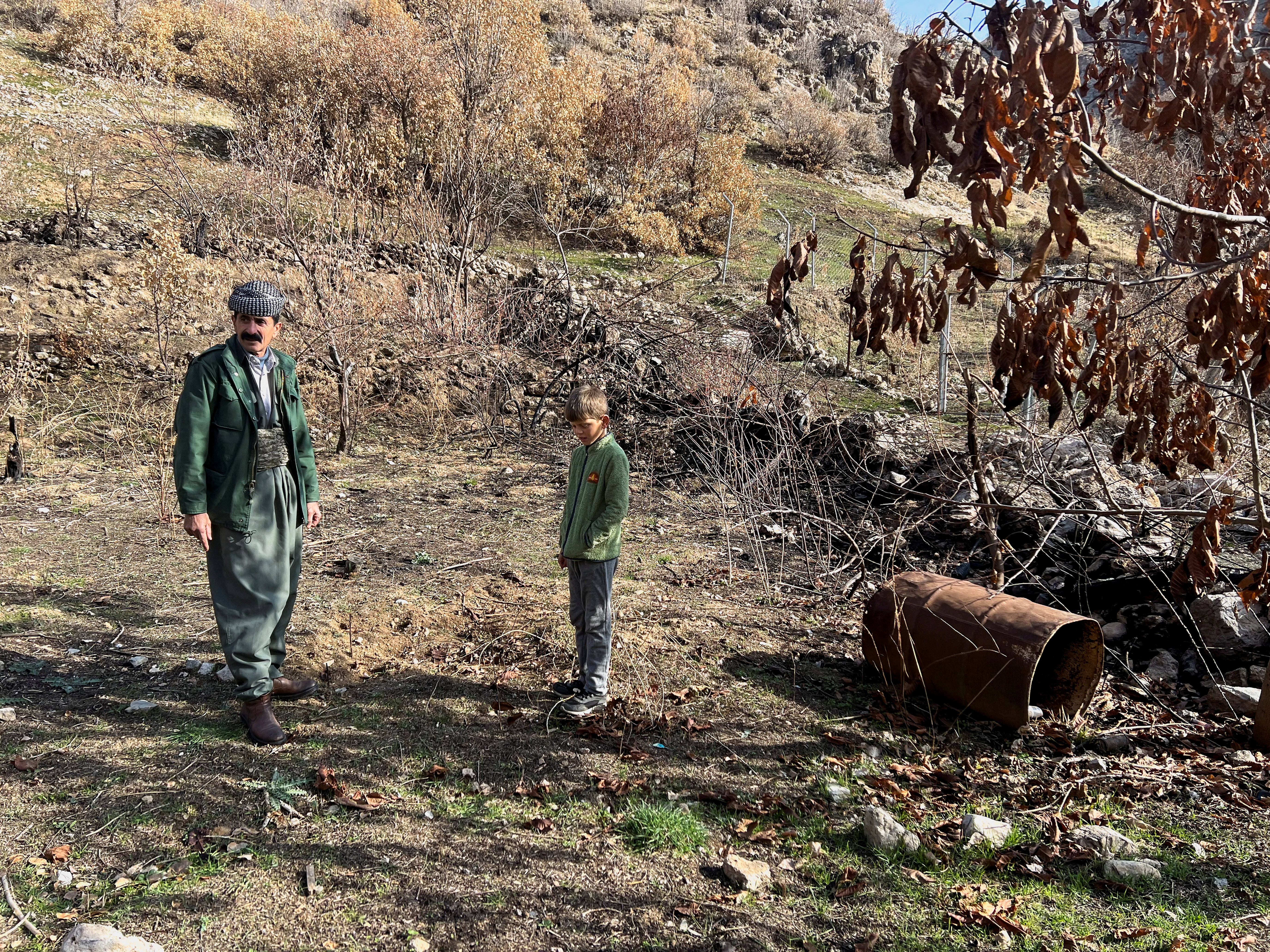 Omar Abdullah Qasim stands with his grandson in the yard next to his house in Sararo village, where he claims several rockets landed during the Turkish bombardment last year, in Dohuk