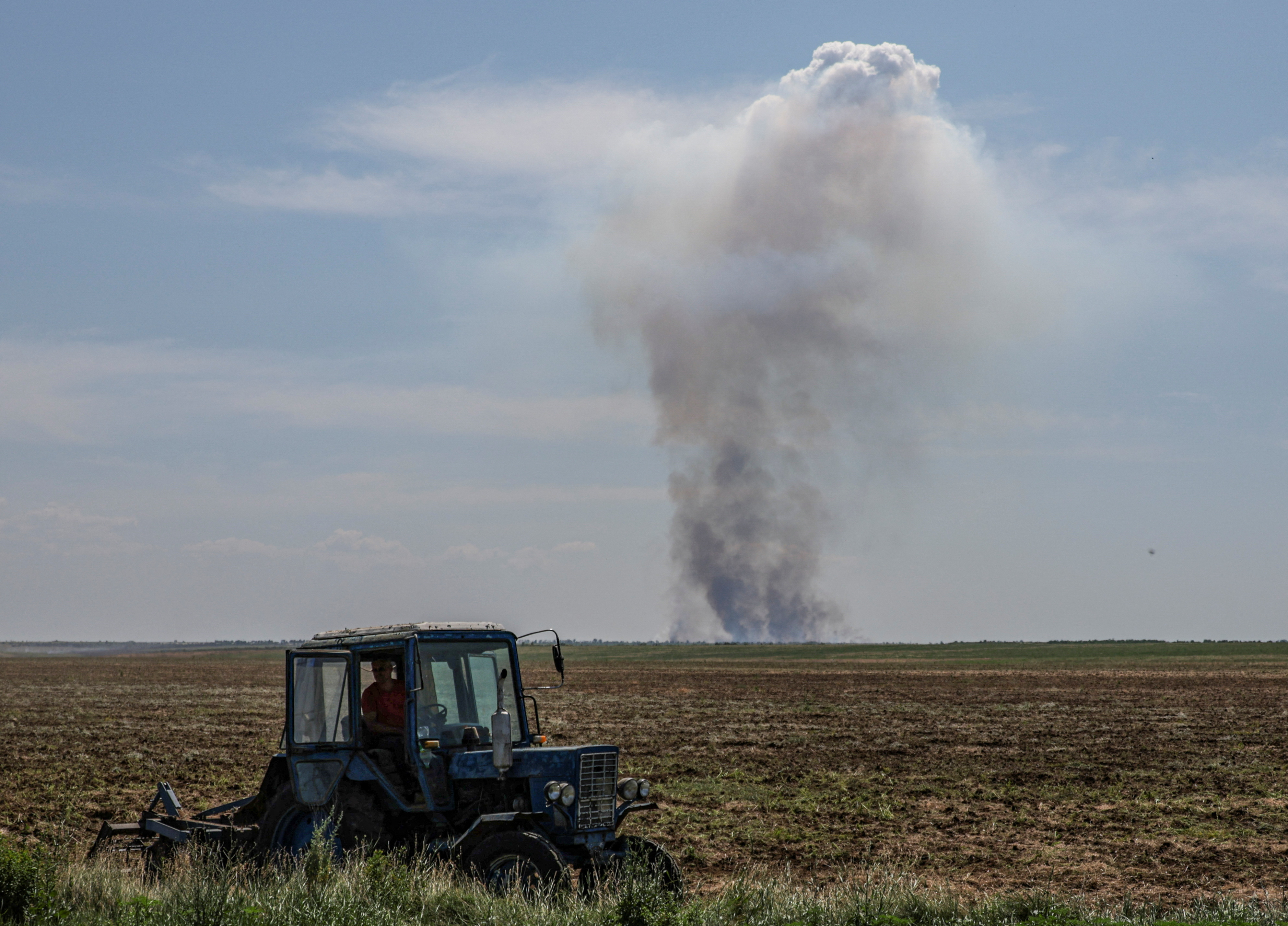 Agricultural worker operates a tractor as smoke rises in the distance after a military strike in Kherson region