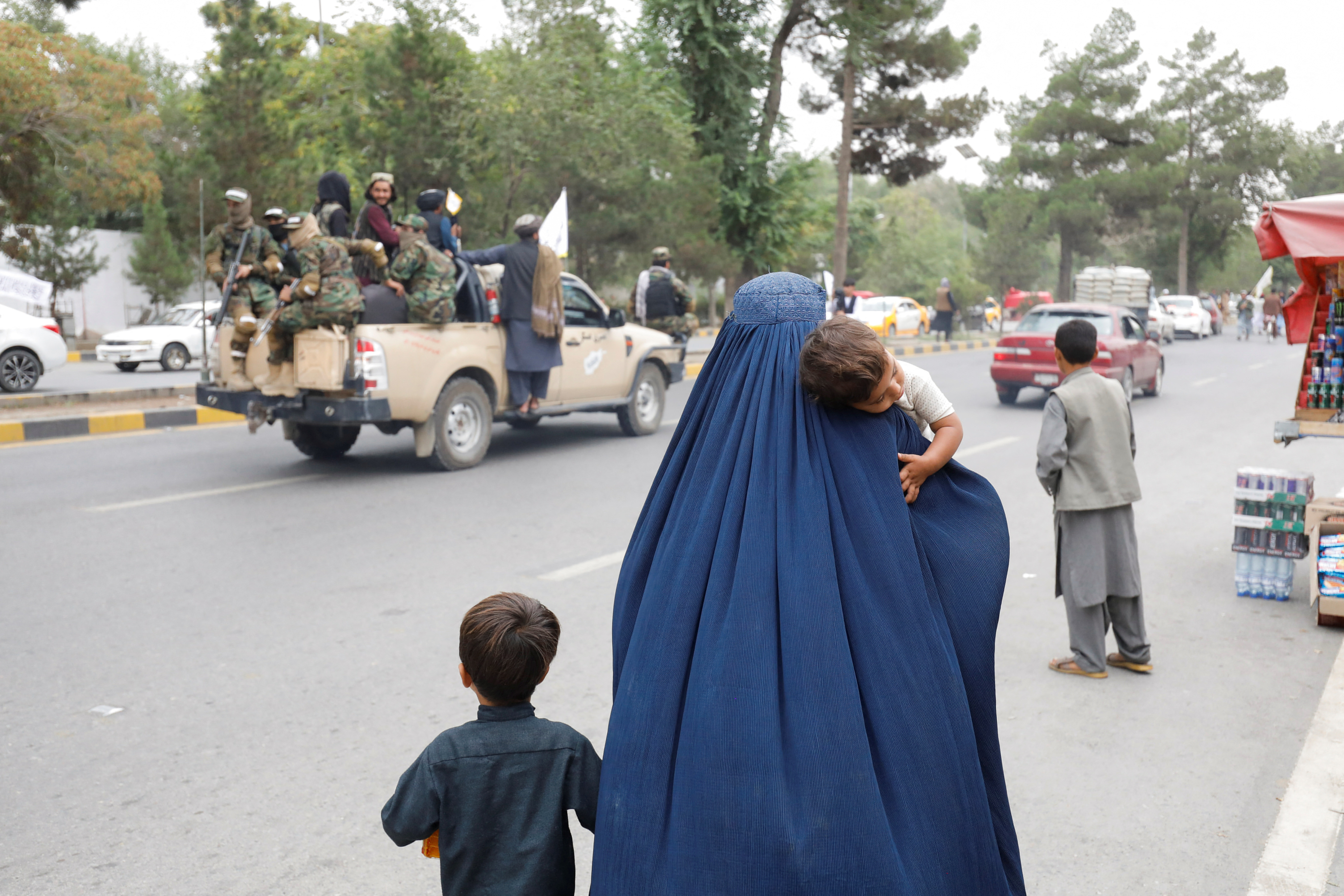 An Afghan woman walks with her children on the anniversary of the fall of Kabul on a street in Kabul