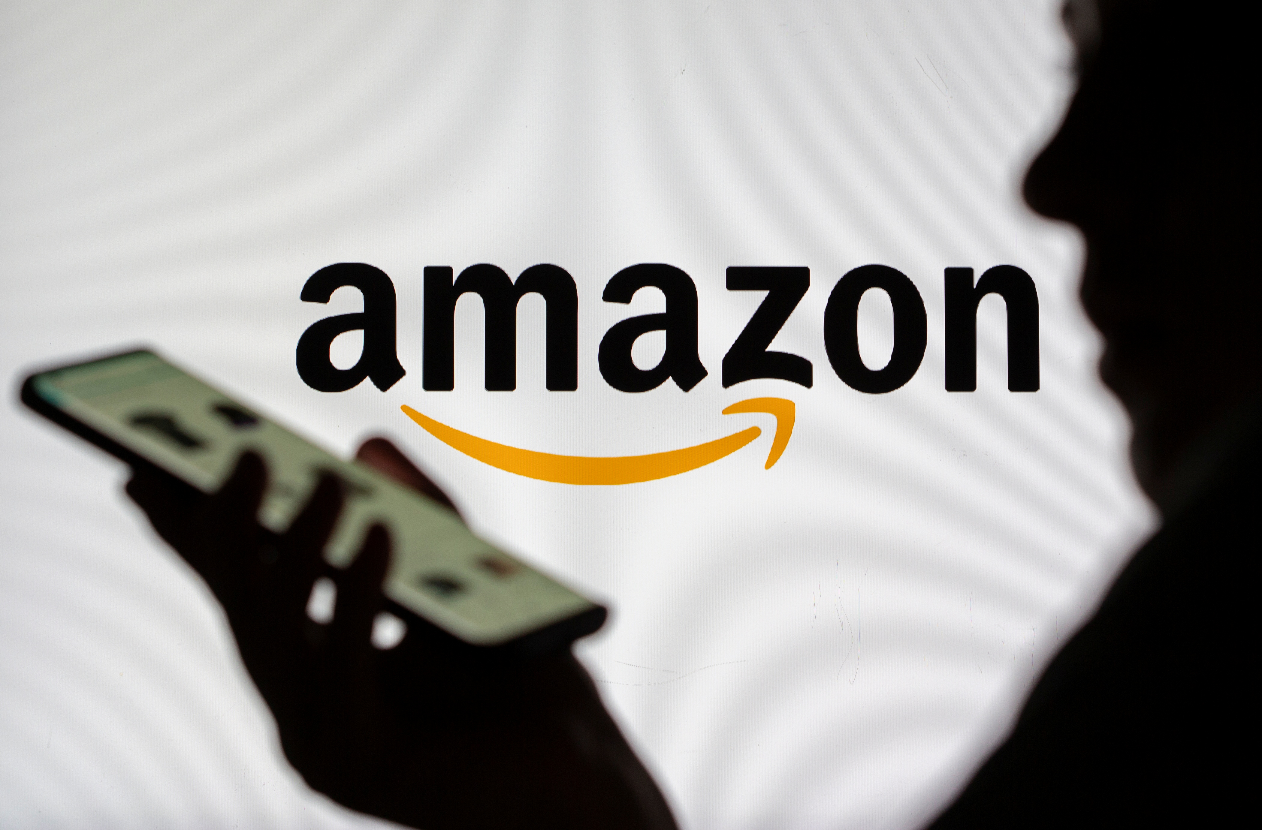 Woman with smartphone is seen in front of displayed Amazon logo in this illustration taken