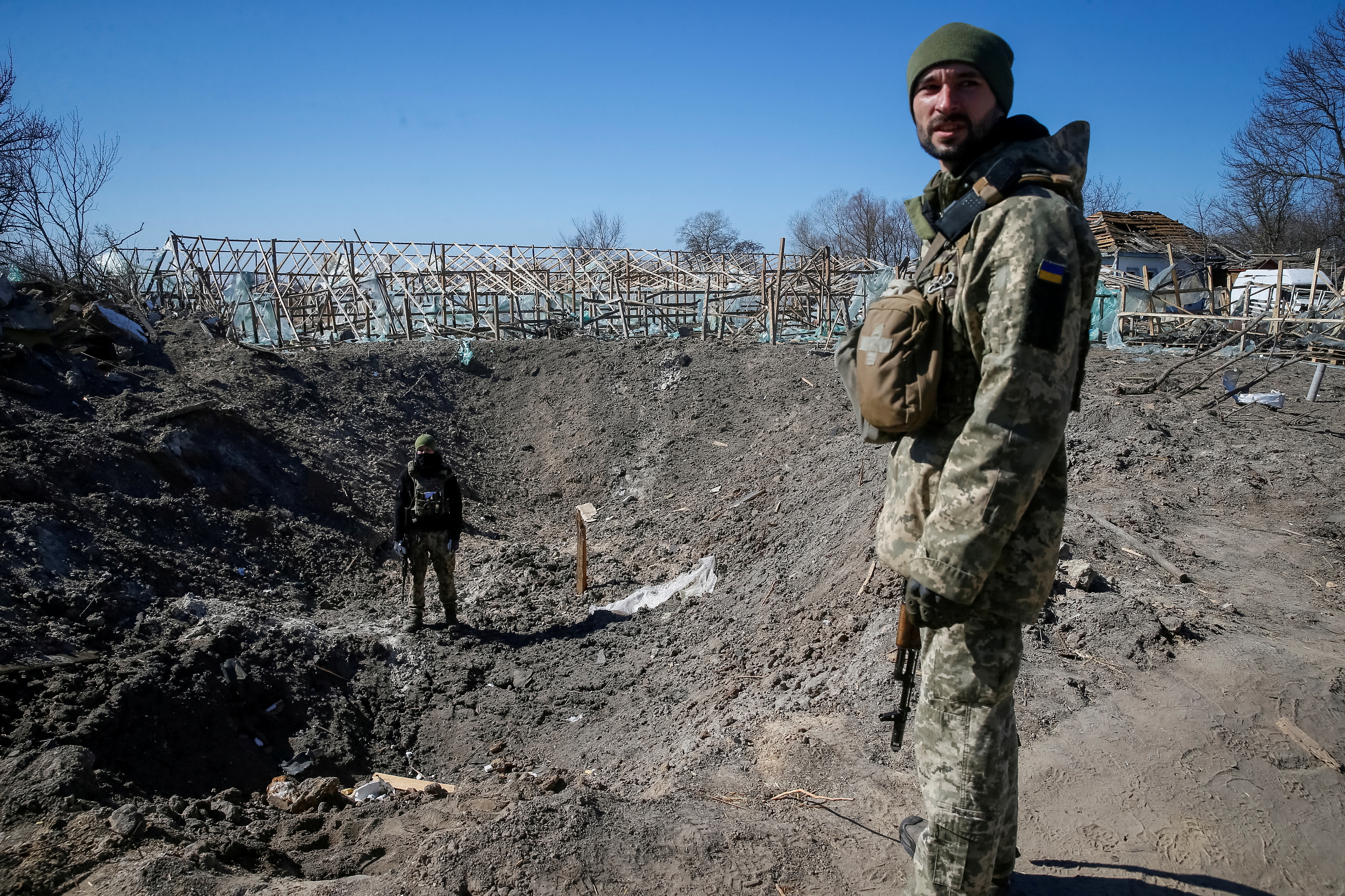 Ukrainian service members inspect a shell crater in a village on the front line in the east Kyiv region