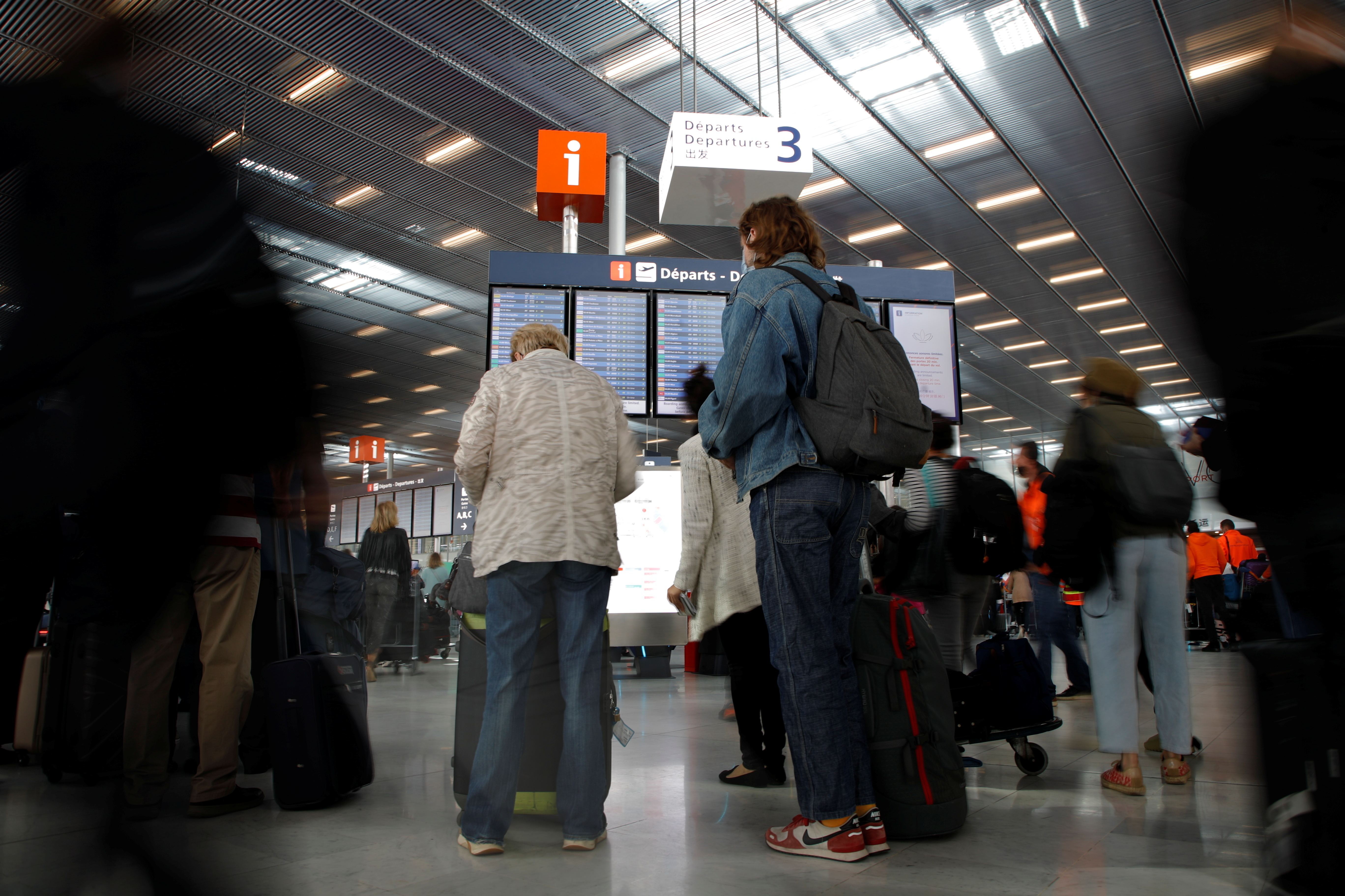 Passengers stand in front of a departures board at Orly Airport